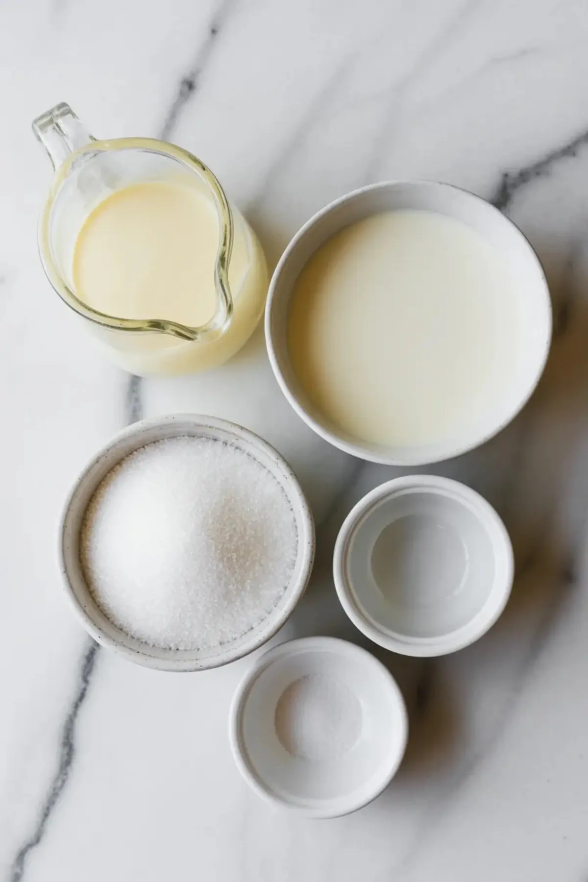 Cotton candy ice cream ingredients sit on a marble surface with cream, milk, sugar, vanilla, and salt measured for a homemade ice cream treat.