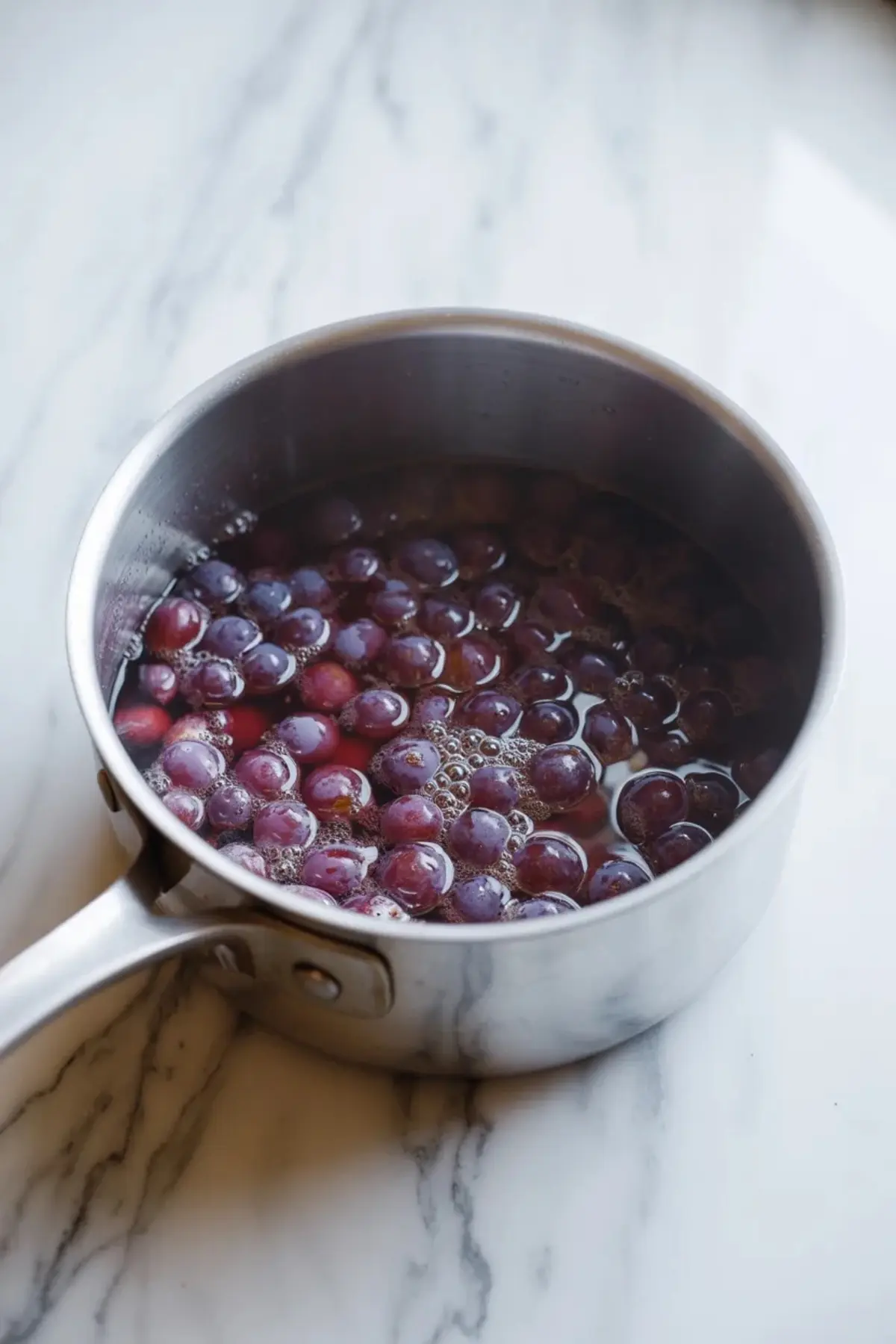 Fresh grapes simmering in a saucepan to build the fruit base for homemade grape ice cream.