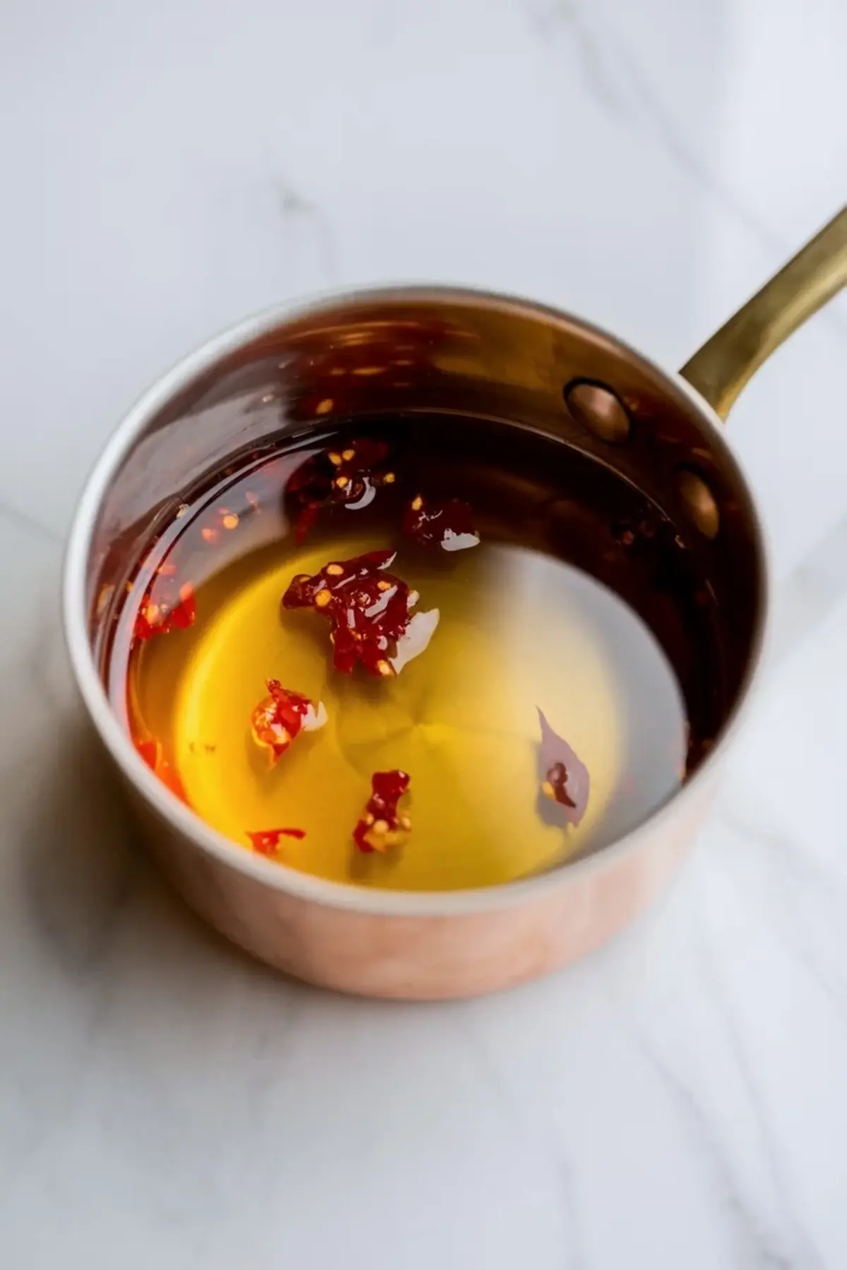 Hot honey sits in a small saucepan with red pepper flakes, showing the warm honey drizzle used for the cornbread muffins.