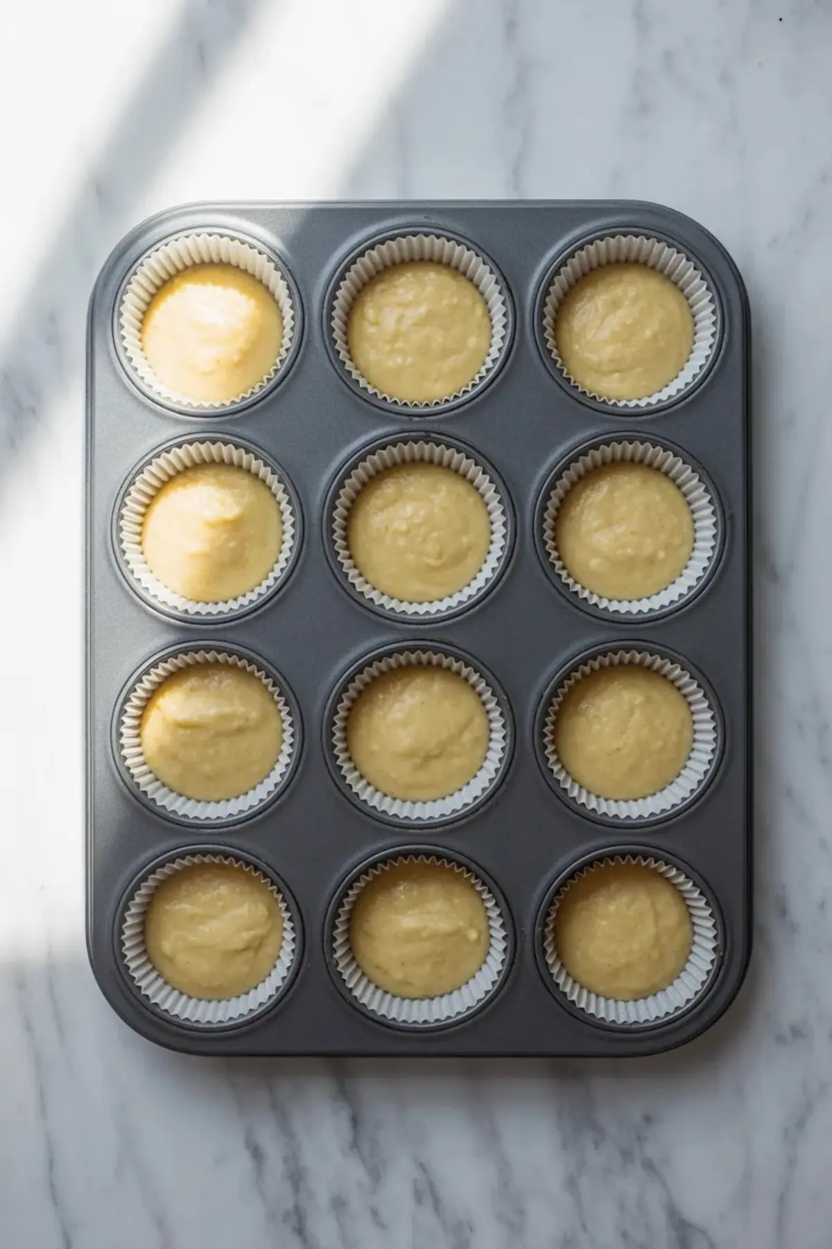 Cornbread muffin batter fills a lined muffin pan before baking, showing the soft pale batter portioned evenly into each cup.