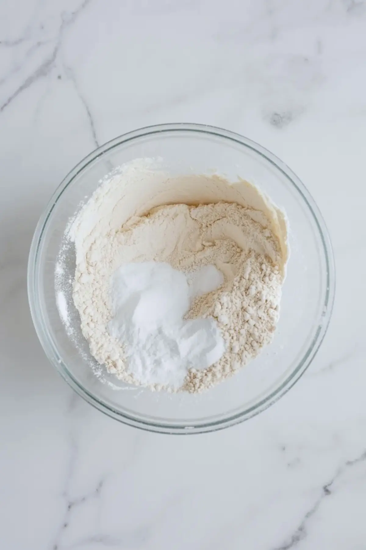 Dry ingredients for lavender sour cream cookies in a glass bowl with flour, baking powder, baking soda, and salt before mixing.