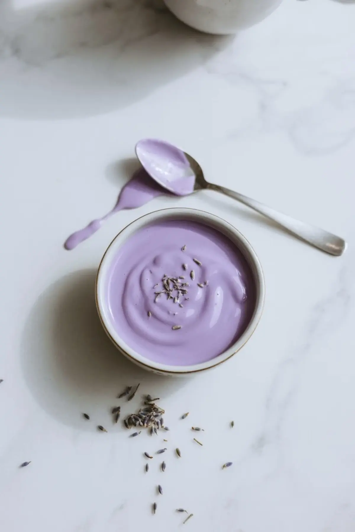 Lavender glaze for sour cream cookies in a small bowl with a spoon and dried culinary lavender on the marble surface.