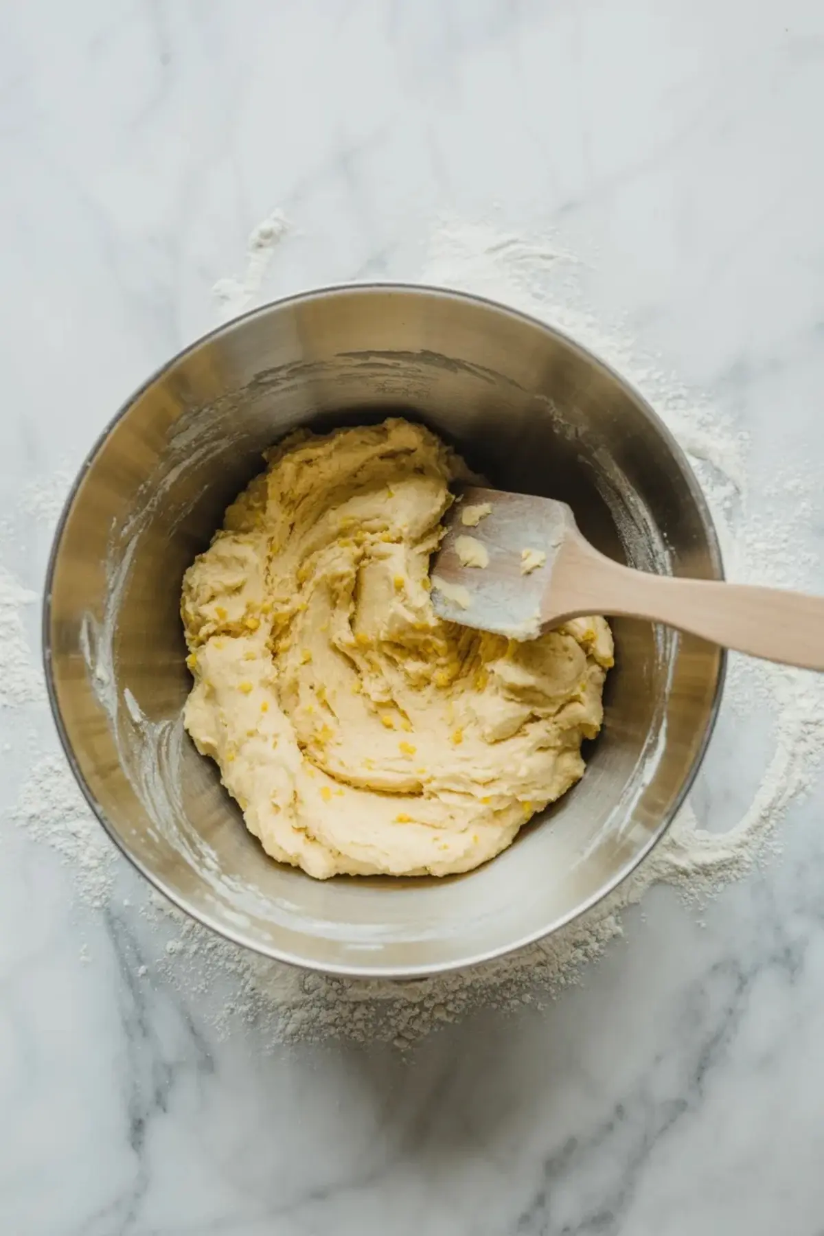 Cookie dough for lemon cheesecake cookies with ricotta mixing in a glass bowl on a marble surface.