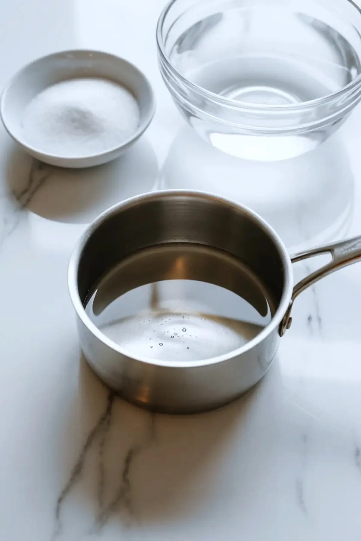 Simple syrup ingredients with sugar, water, and a saucepan arranged on white marble for fresh lemon sorbet.