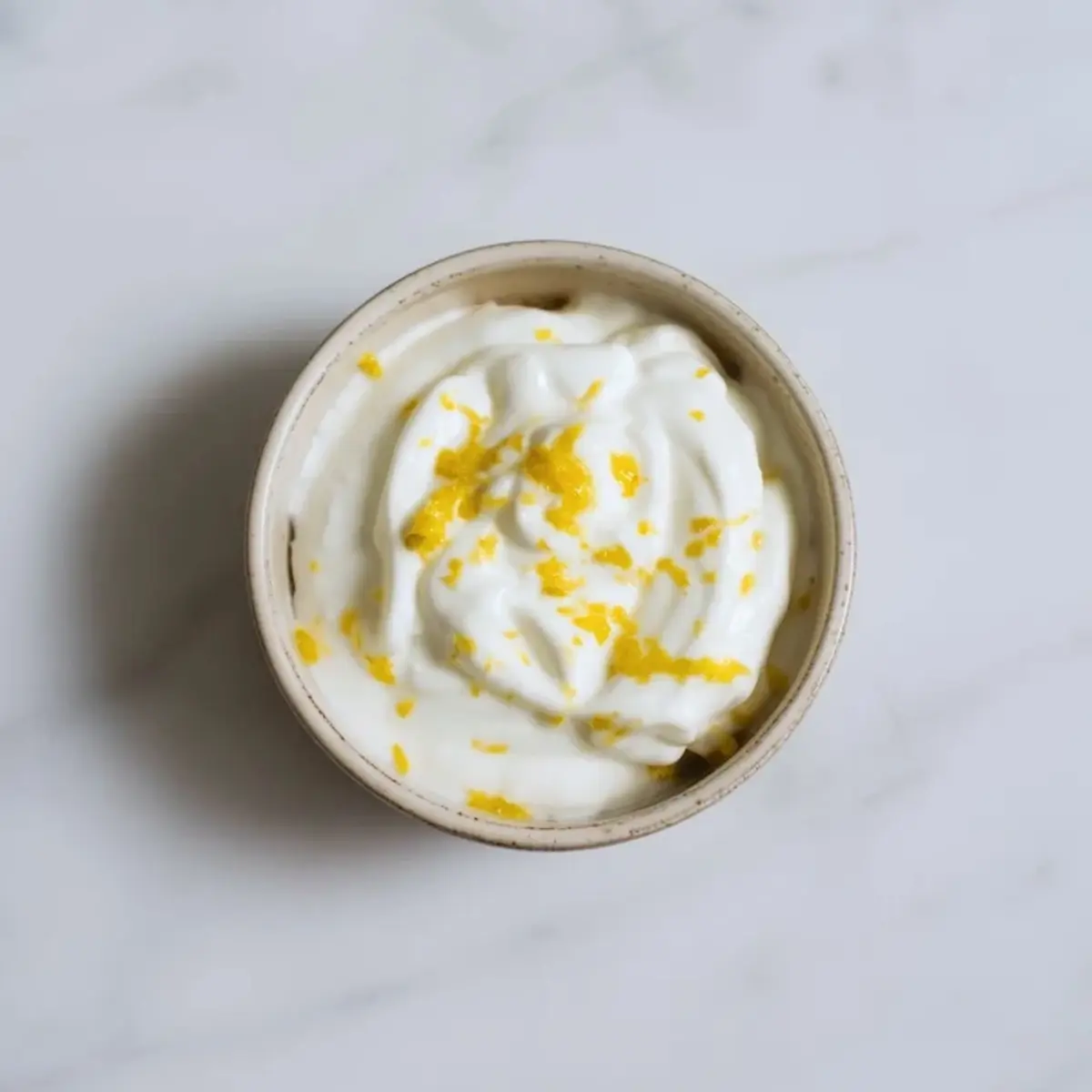 Greek yogurt mixed with fresh lemon zest for lemon yogurt parfait in a small bowl.
