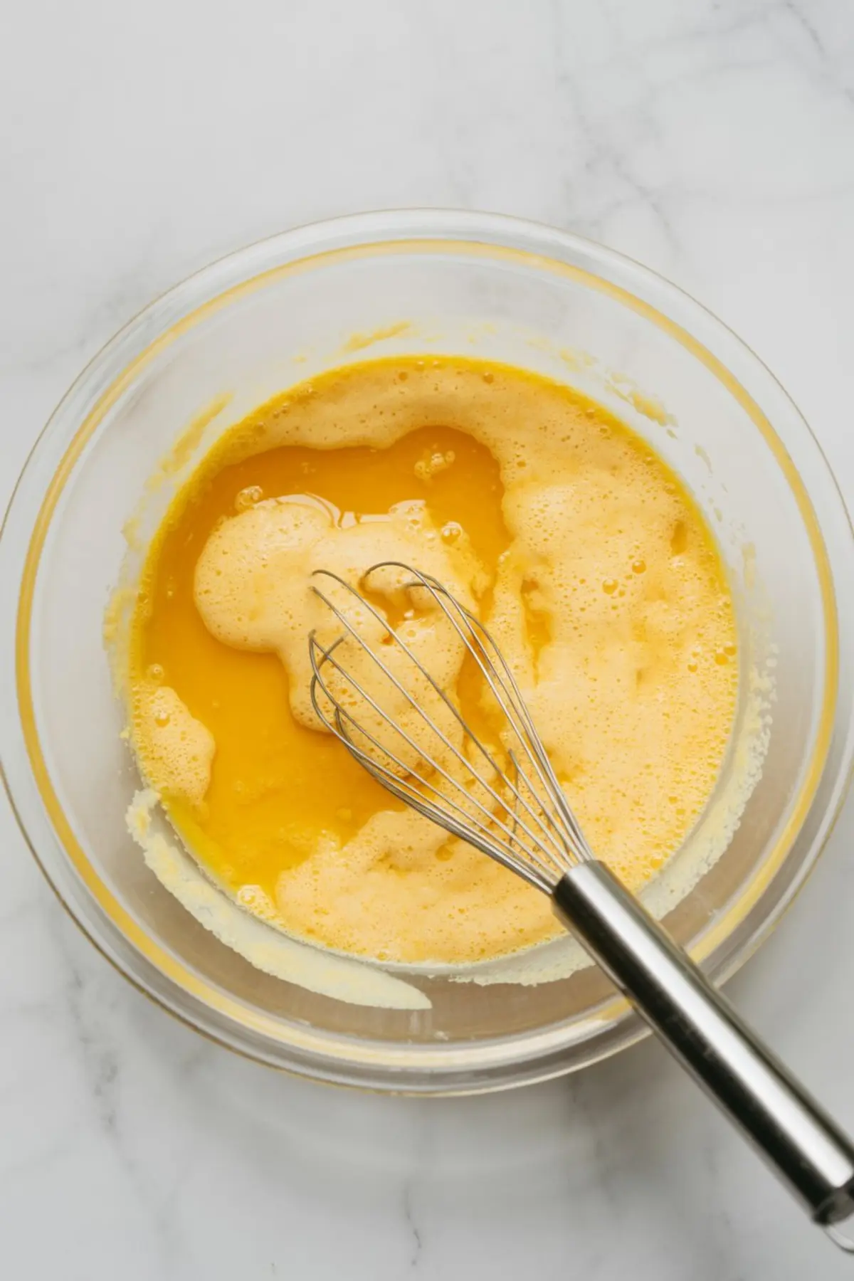 Orange chiffon cake wet ingredients are whisked in a glass bowl until smooth and evenly combined.