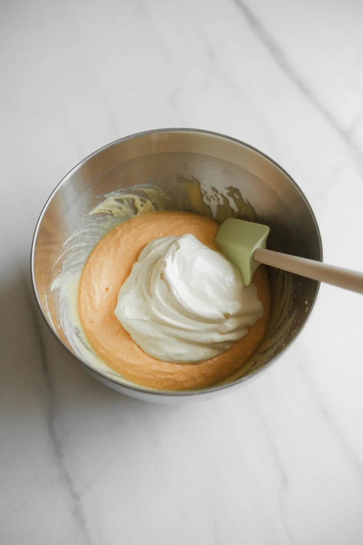 Whipped egg whites are folded into orange chiffon cake batter with a spatula to keep the mixture airy.