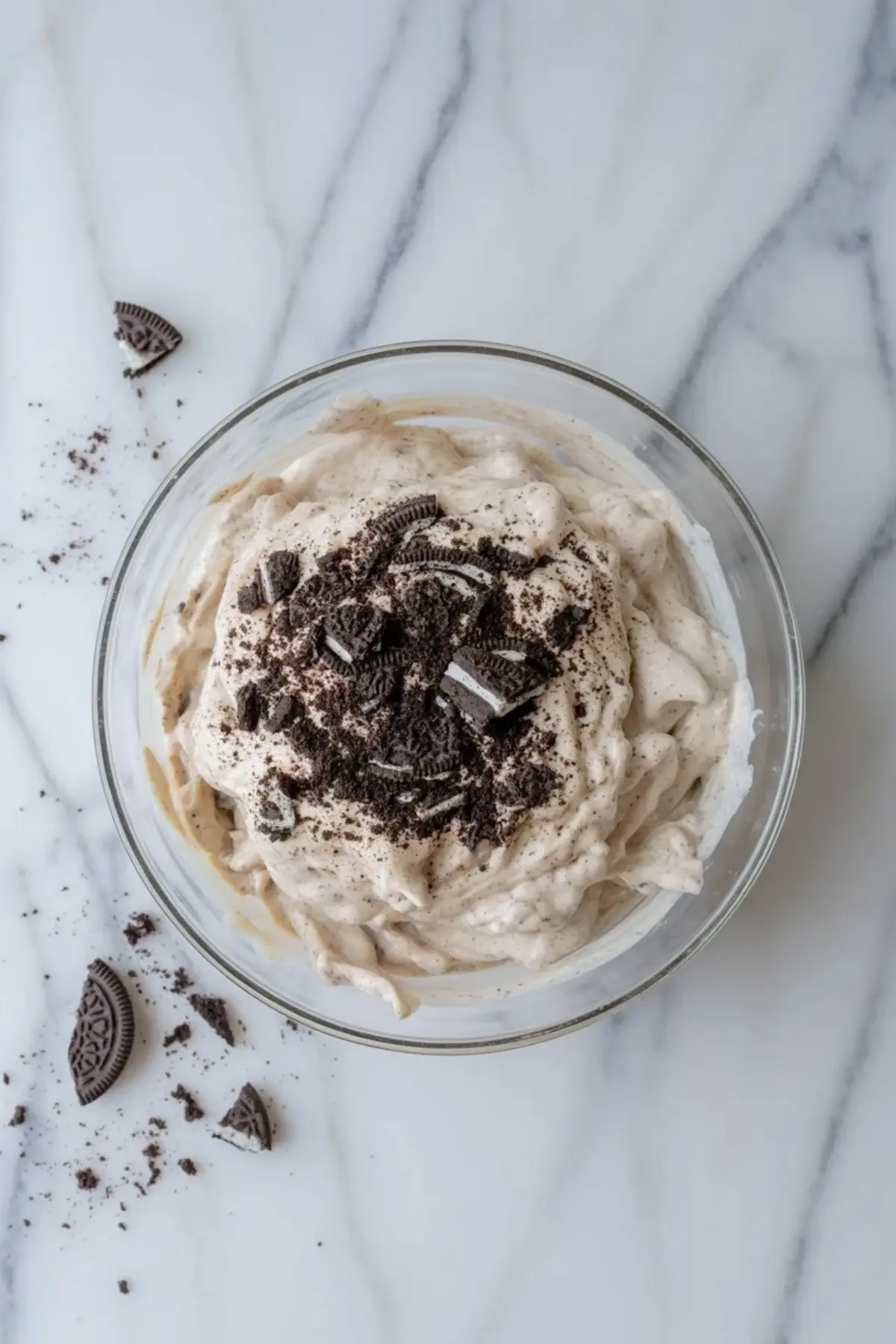 Finished Oreo mousse in a glass bowl topped with crushed Oreo cookie pieces, showing the creamy cookies and cream texture on white marble.