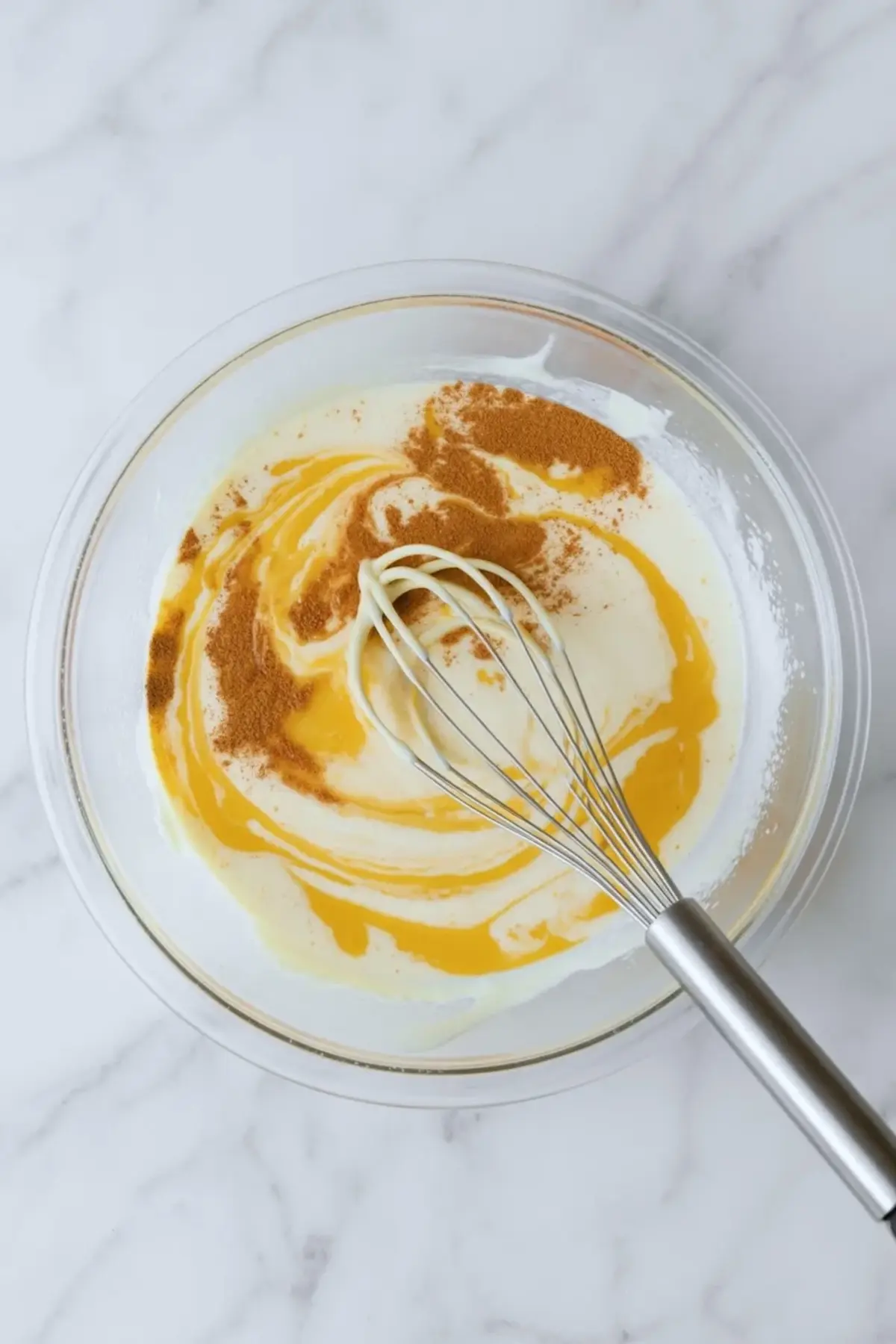 Vanilla cinnamon custard for strawberry French toast casserole being whisked in a glass bowl.