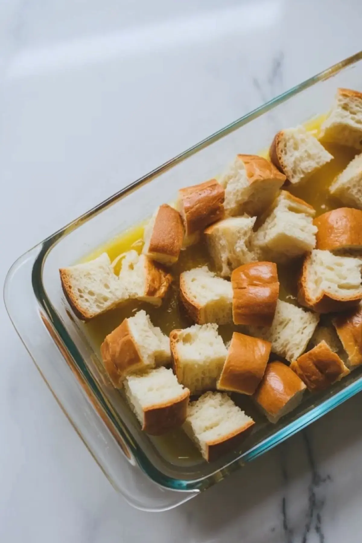 Cubed brioche soaking in custard in a baking dish for overnight strawberry French toast casserole.