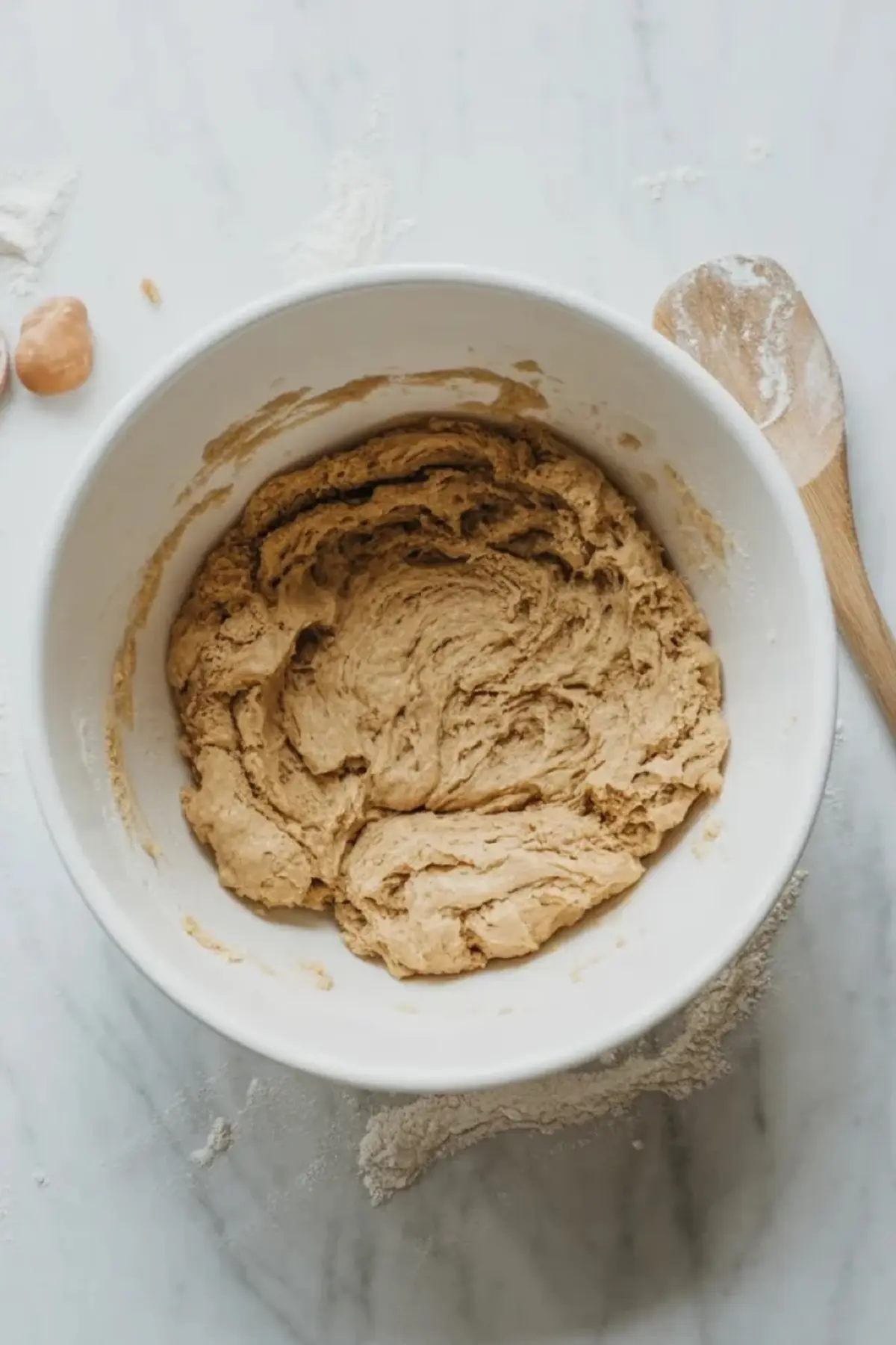 Mixed peach and thyme cornbread cookie dough sits in a white mixing bowl on a white marble surface before shaping.