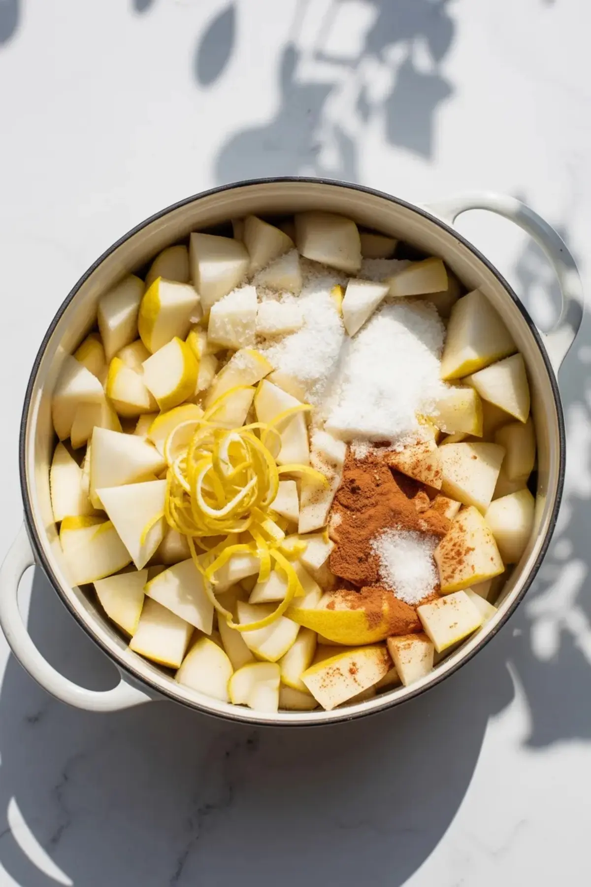 Chopped ripe pears sit in a saucepan with sugar and lemon as the pear jam recipe begins, with the fruit filling most of the pan.