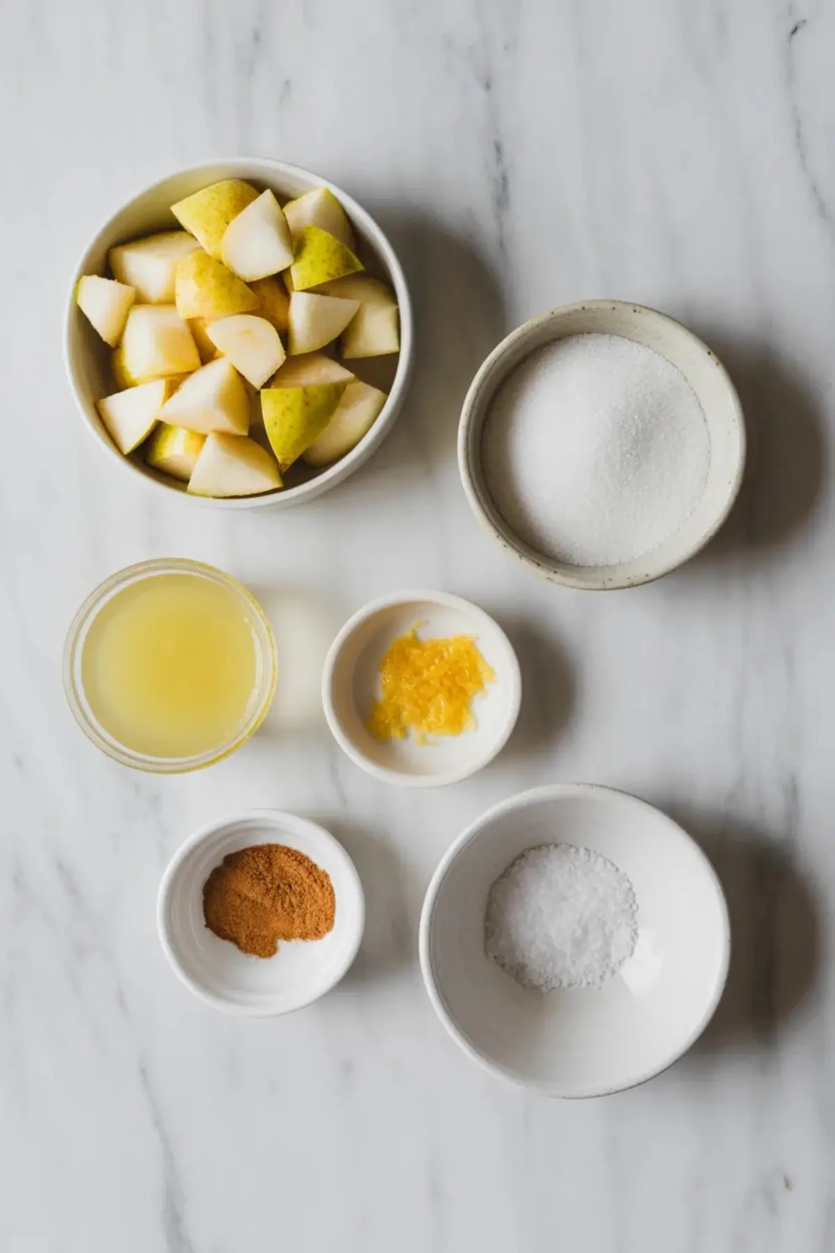 Fresh ripe pears sit whole on a marble surface beside a knife and wooden board, showing the fruit used for homemade pear jam.