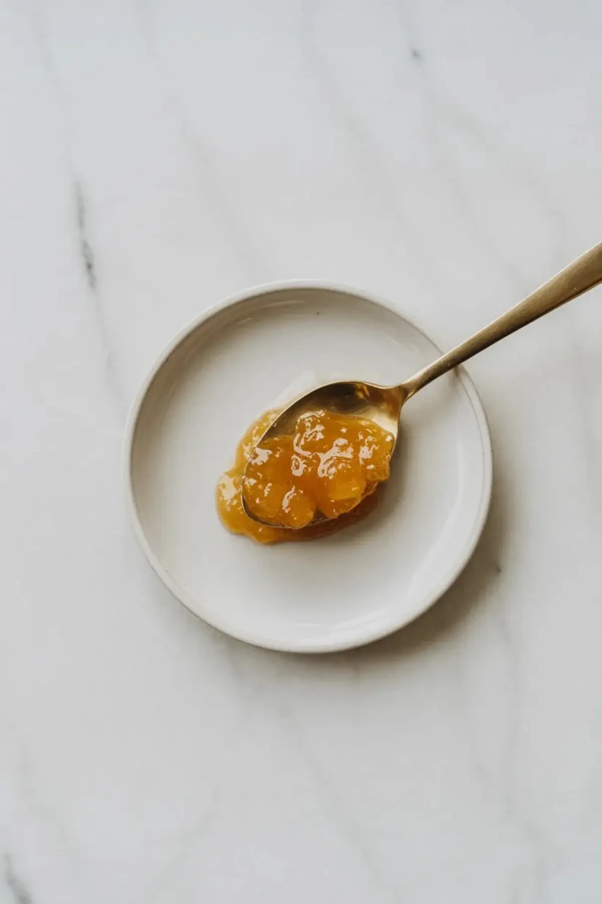 Jar of pineapple jam with a biscuit topped with pineapple jam beside it.