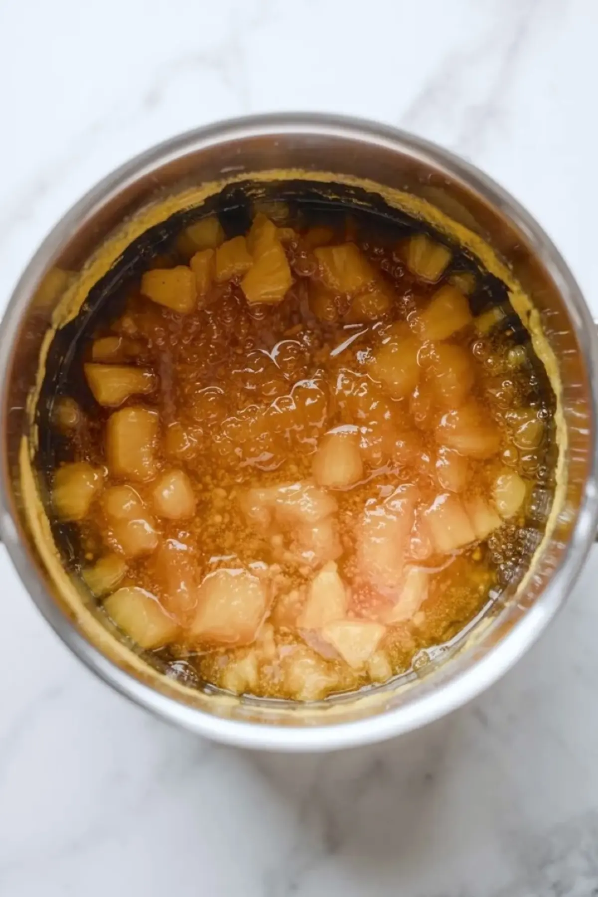 Ingredients for pineapple jam arranged on a marble surface with pineapple, sugar, lemon juice, zest, and vanilla.