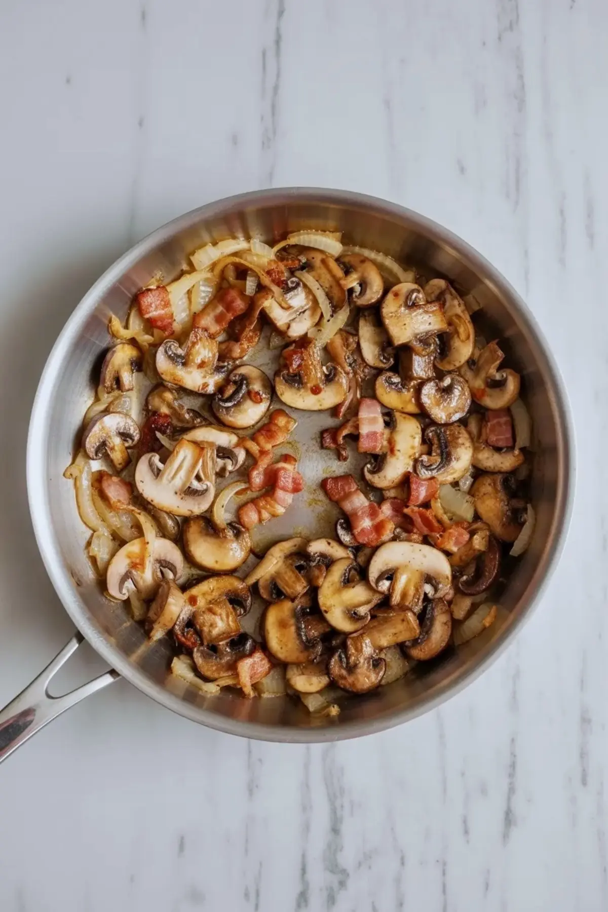 Sliced mushrooms, diced onion, and bacon cook together in a skillet on a marble surface for quiche lorraine with mushrooms, showing the browned savory filling before it goes into the crust.