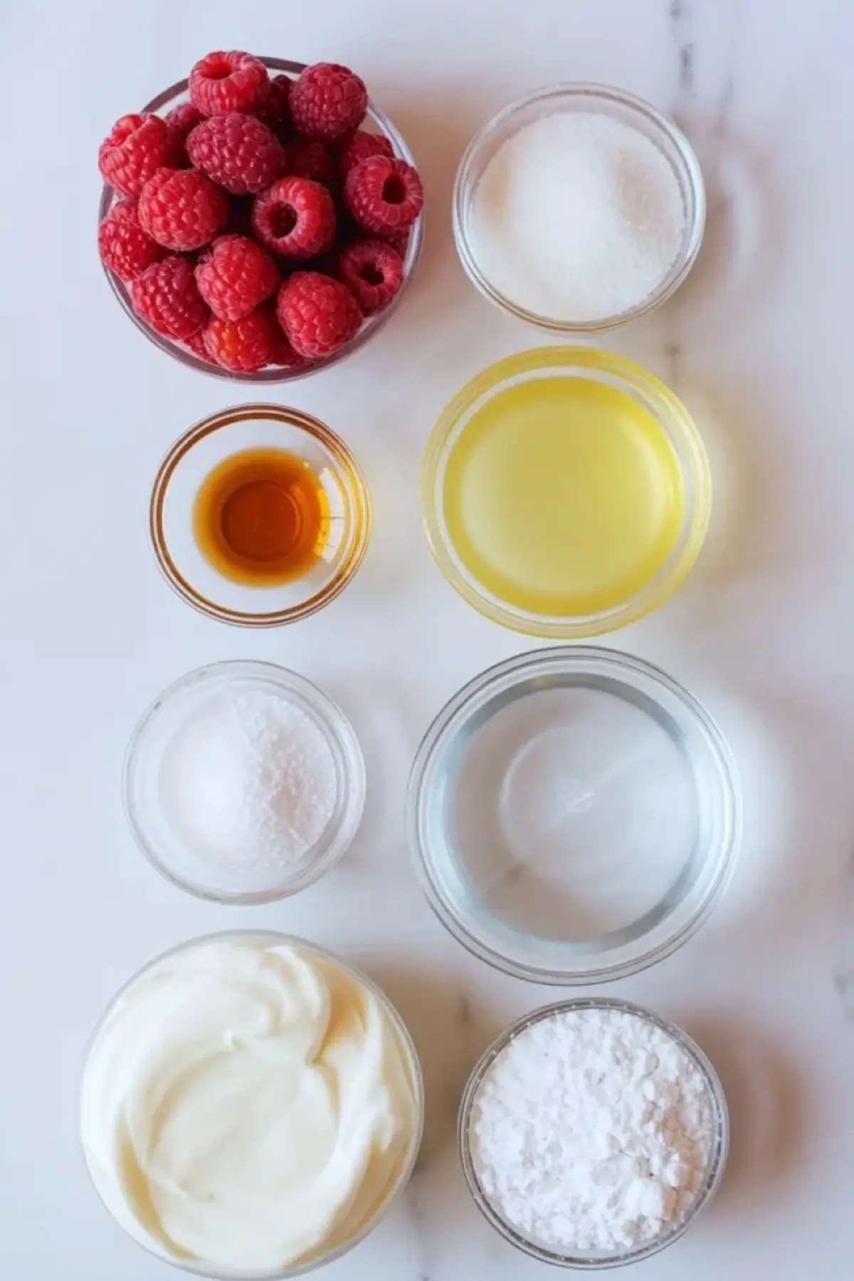 Ingredients for raspberry mousse filling arranged on white marble with raspberries, cream, sugar, lemon juice, vanilla, gelatin, and powdered sugar.