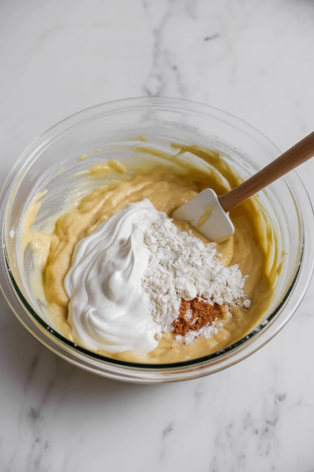 Rhubarb coffee cake batter in a glass bowl with sour cream, flour, and cinnamon ready to be folded in.