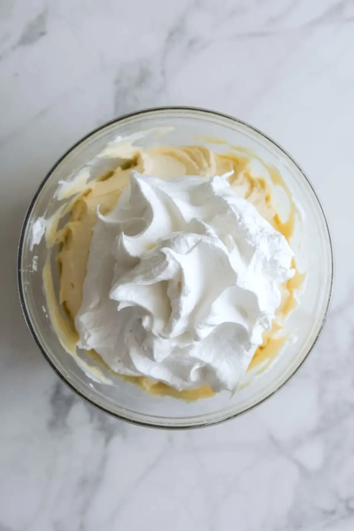 Whipped topping piled over the strawberry cheesecake fluff base in a glass bowl before the mixture is folded together.