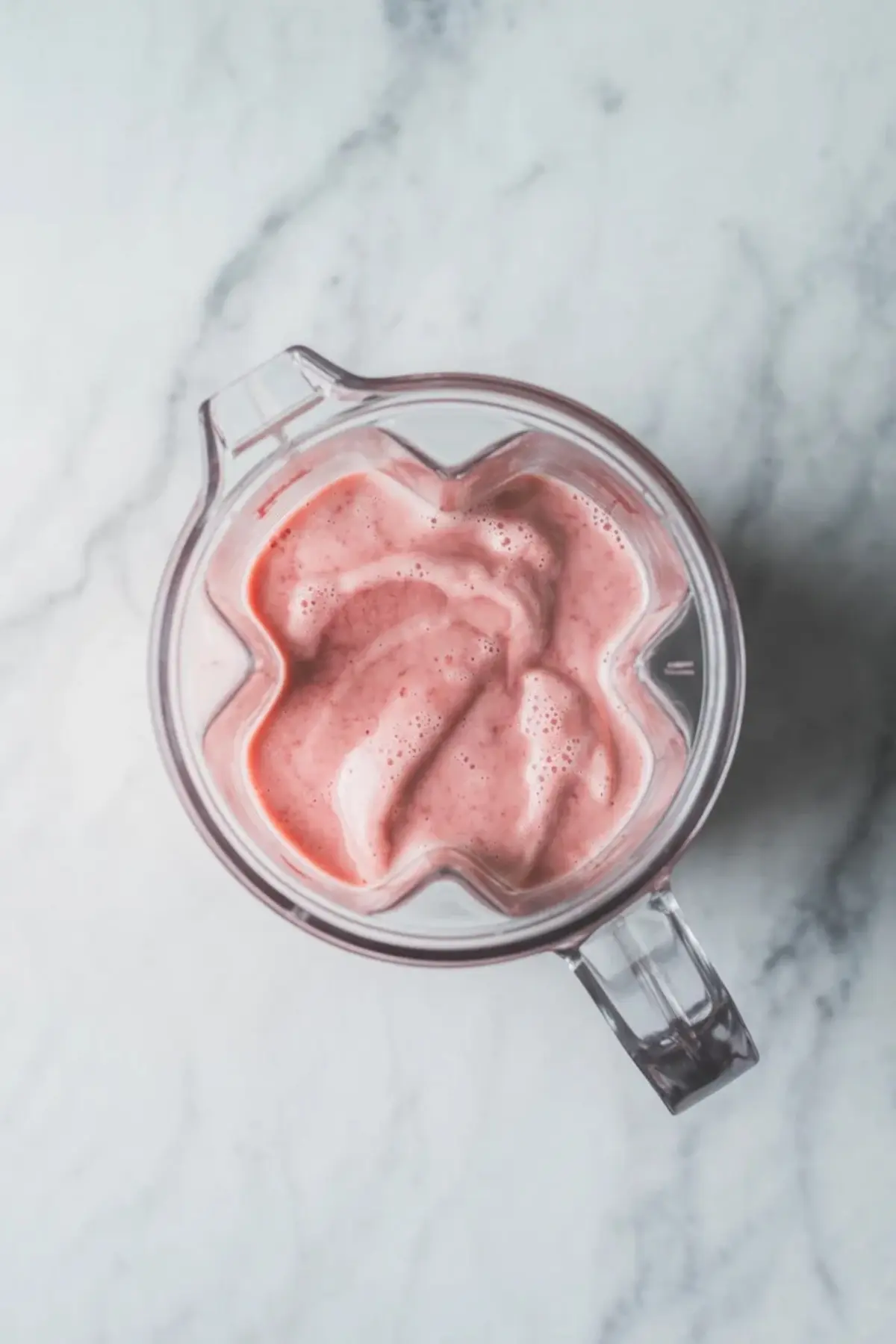 Top view of a blender jar filled with smooth pink strawberry smoothie mixture used as the base for strawberry chia seed pudding.