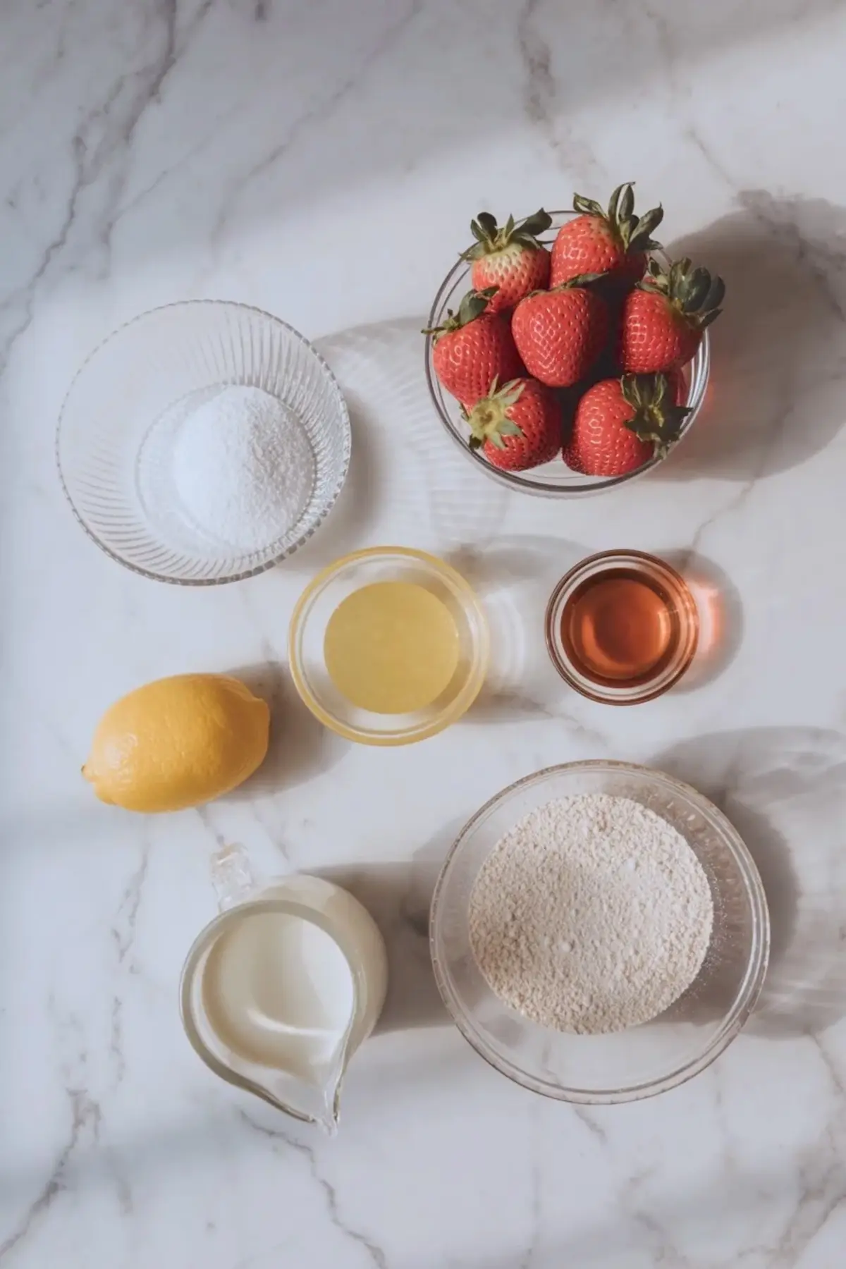 Ingredients for strawberry mousse cake filling arranged with fresh strawberries, sugar, lemon, vanilla, cream, and gelatin on white marble.