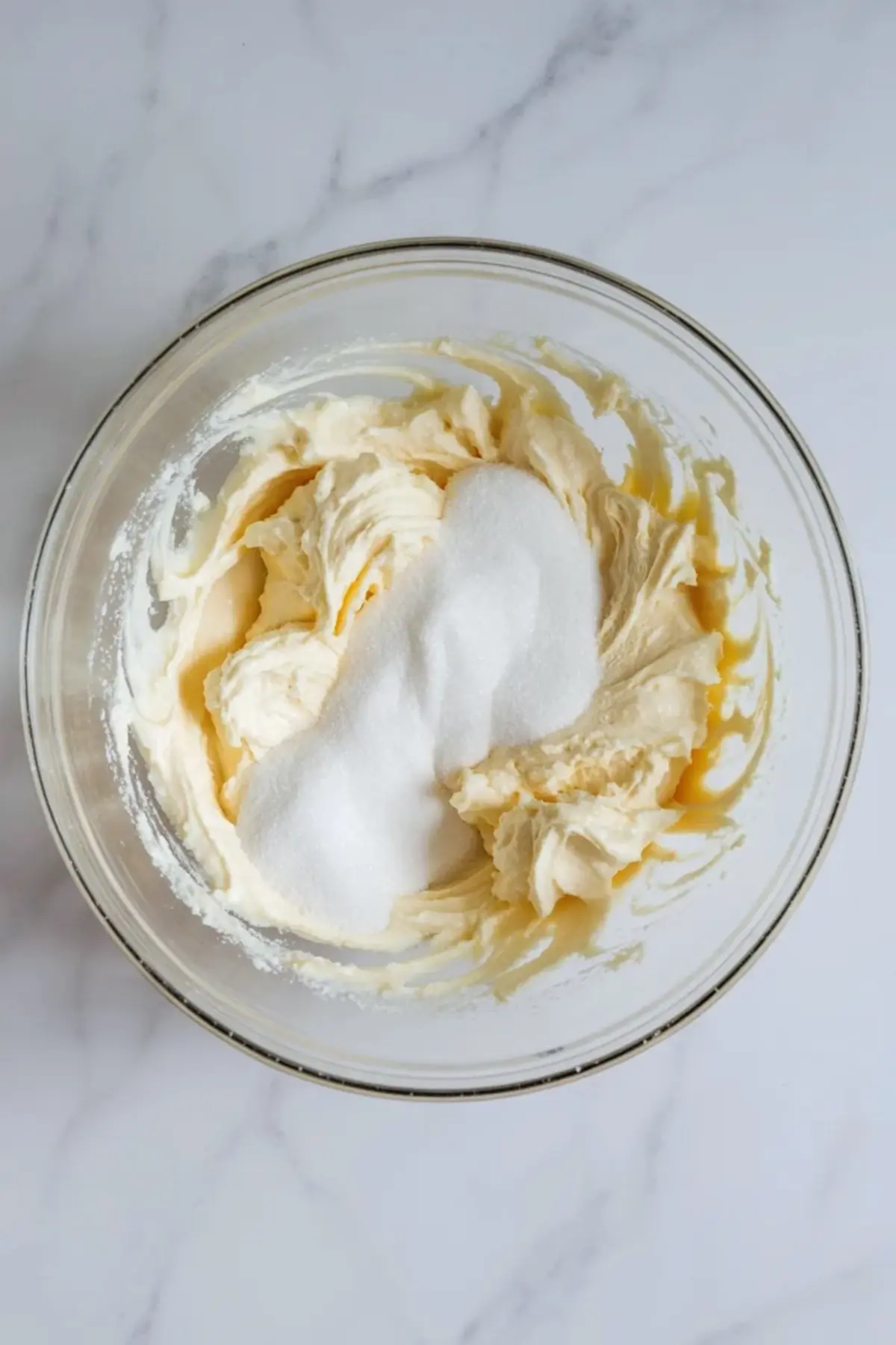 Softened cream cheese with sugar in a glass mixing bowl before it is beaten smooth for strawberry pretzel fluff.