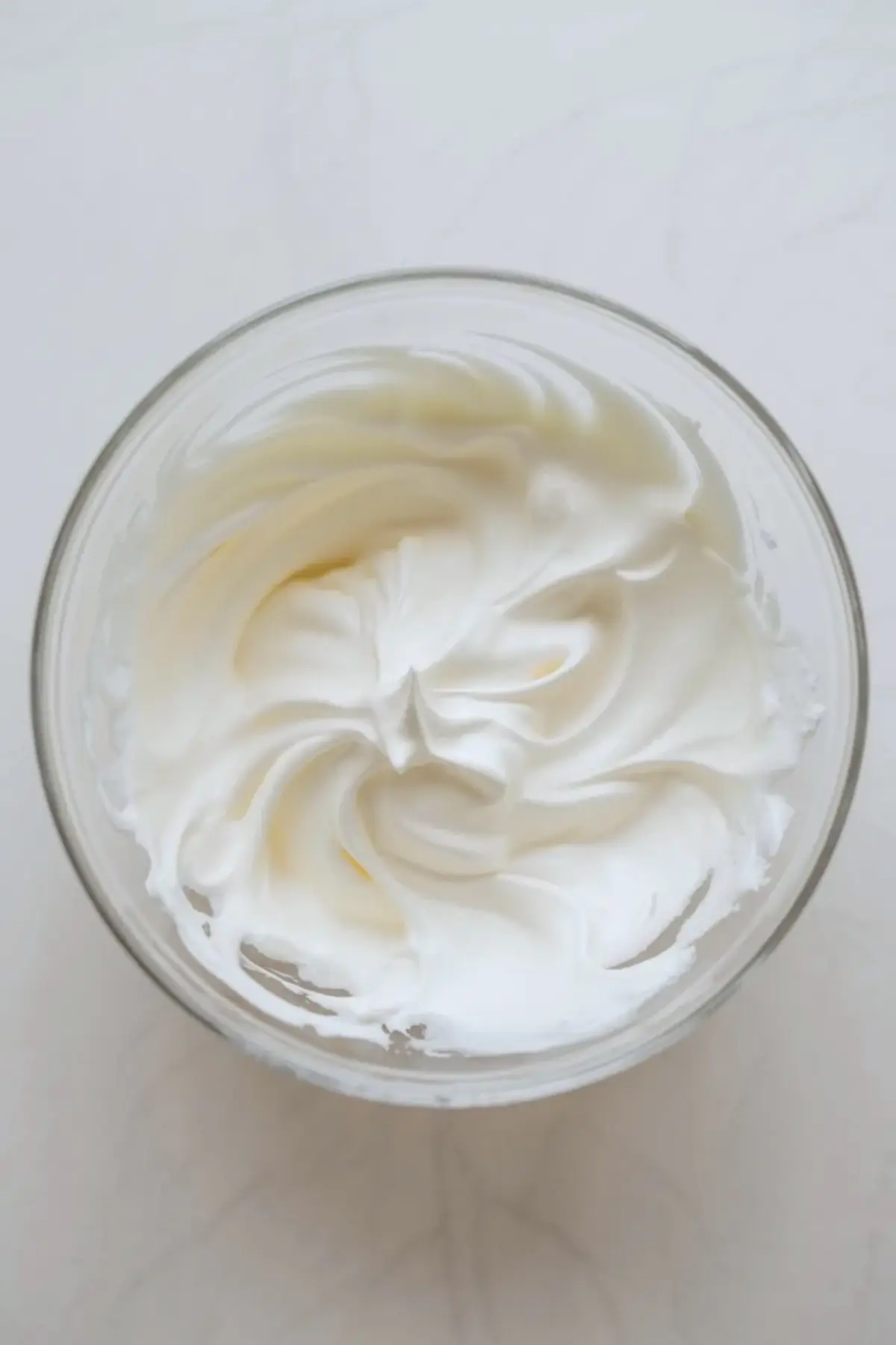 Whipped cream frosting for sheet pan strawberry shortcake cake swirled in a glass bowl before it is spread over the cooled cake.