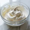 Smooth vanilla mousse cake filling in a clear glass bowl on white marble, showing the airy texture of the finished filling.