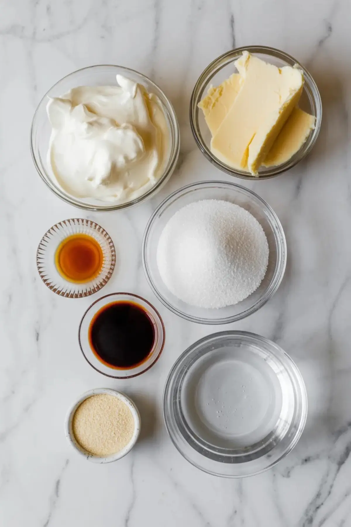 Ingredients for vanilla mousse cake filling arranged with cream, butter, sugar, vanilla, gelatin, and water on white marble.