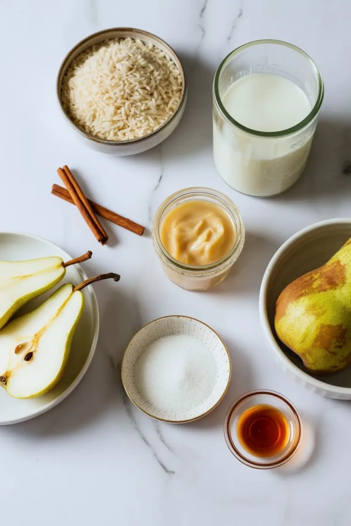 Ingredients for vanilla poached pear rice pudding arranged with short grain rice, milk, condensed milk, pears, vanilla, sugar, and cinnamon.
