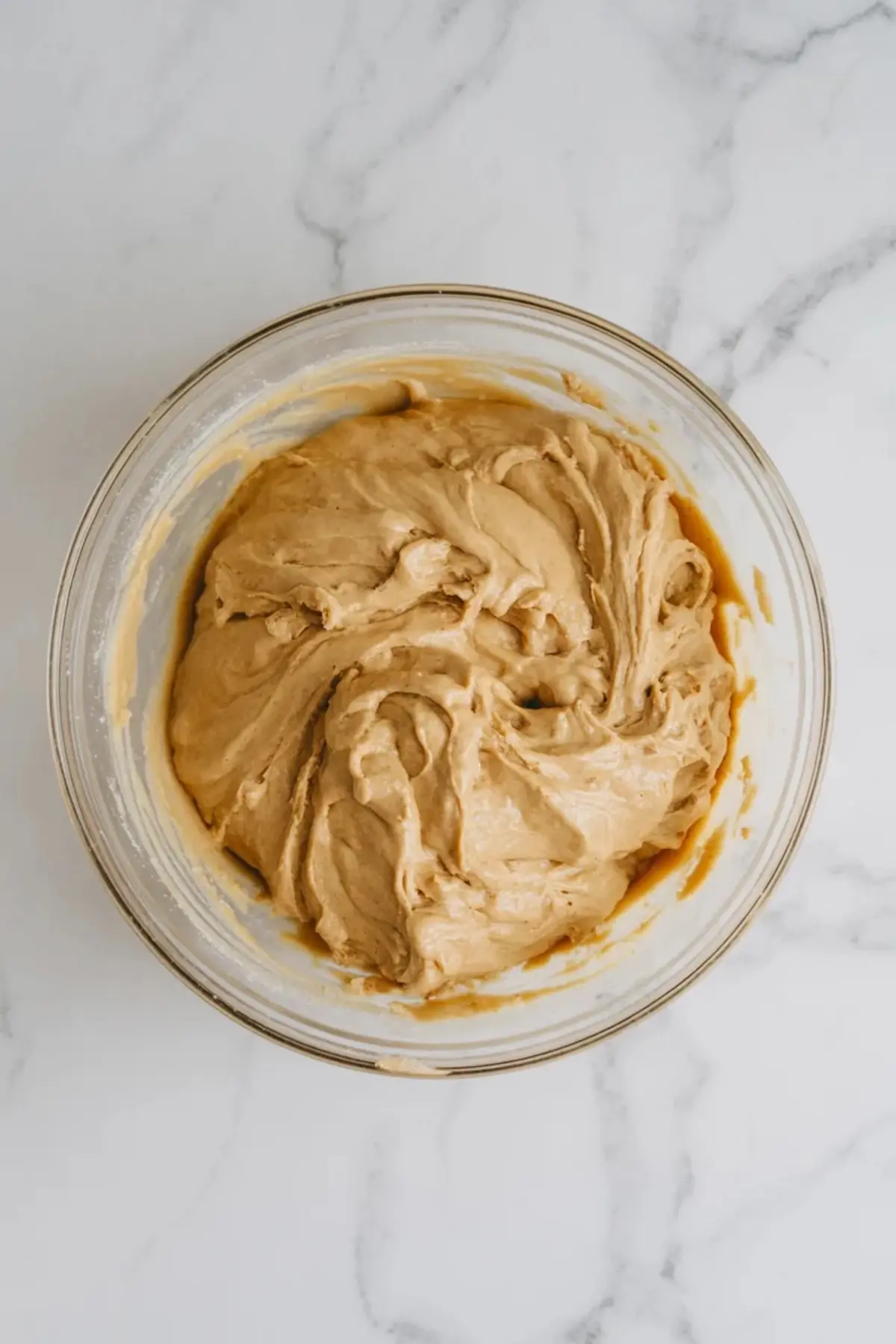 Cookie dough for white chocolate cherry cheesecake cookies mixing in a glass bowl on a marble surface.
