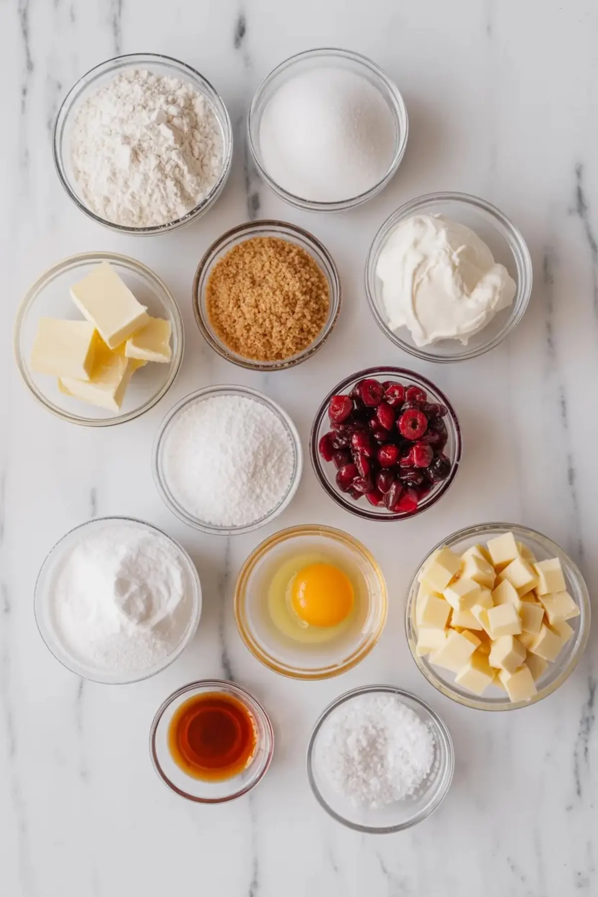 Ingredients for white chocolate cherry cheesecake cookies arranged in bowls with flour, sugar, butter, cream cheese, white chocolate, and cherries.
