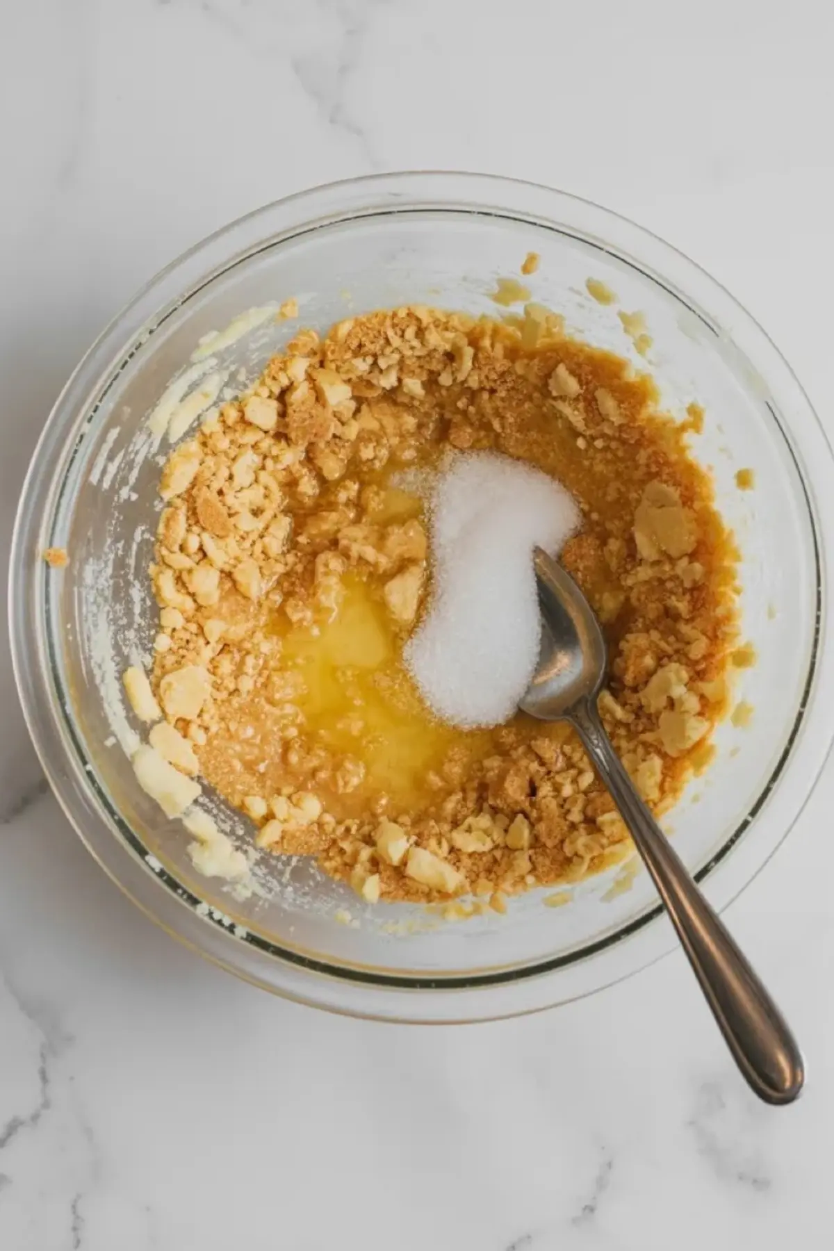 Vanilla wafer crust mixture for no-bake banana pudding bars in a glass bowl with melted butter and sugar on white marble.