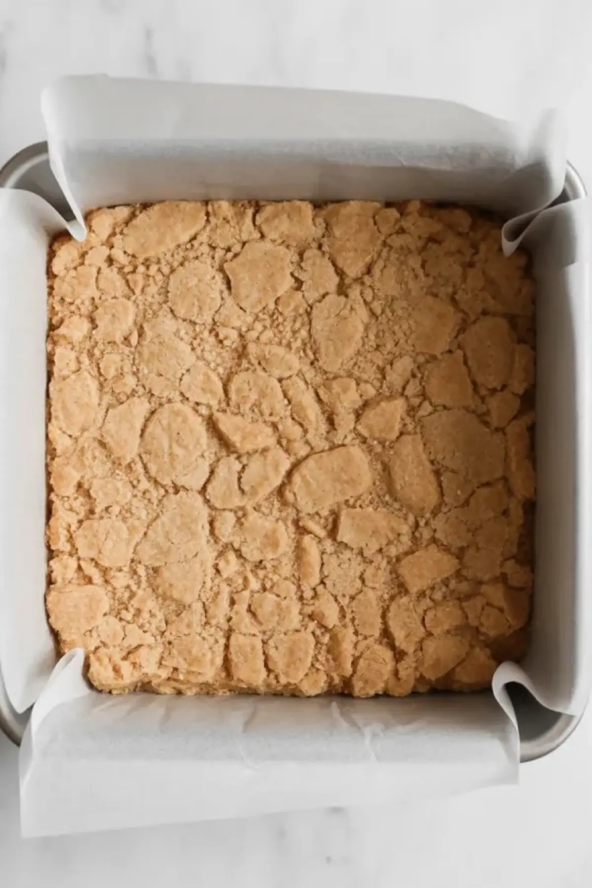 Pressed vanilla wafer crust for no-bake banana pudding bars in a parchment lined square pan on a white marble surface.