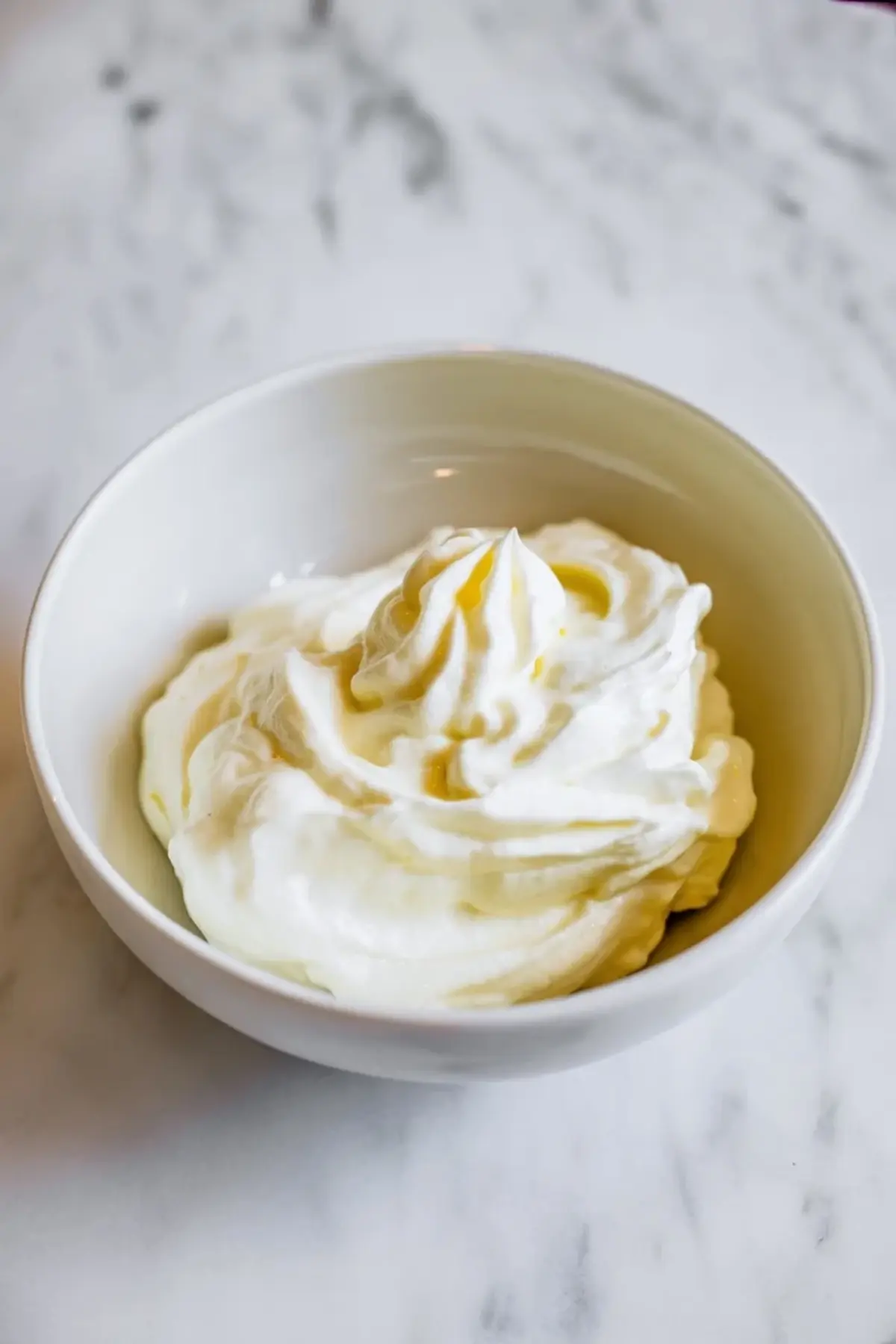 Whipped mascarpone in a small white bowl on marble, showing the soft creamy topping served with blackberry crisp.
