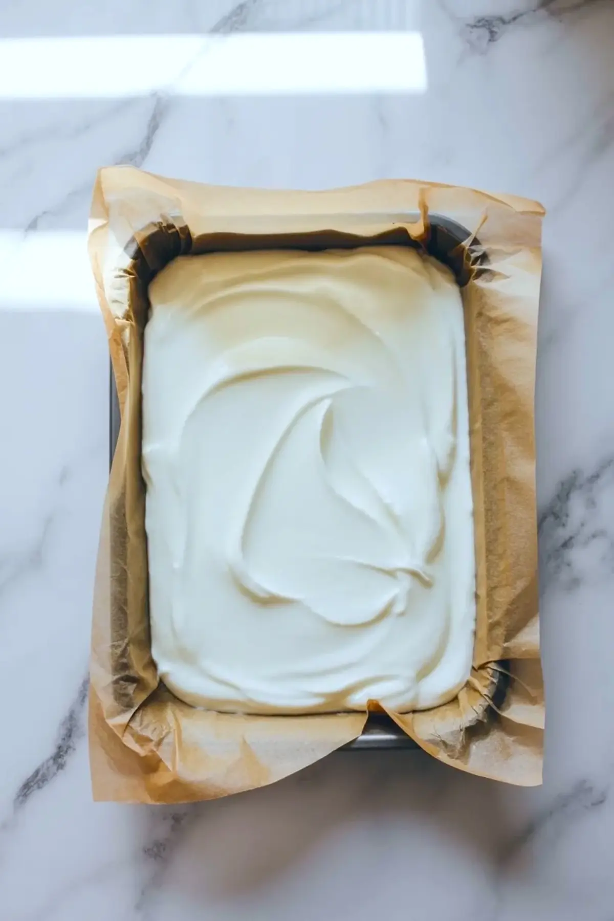 Loaf pan lined with parchment and filled with smooth white yogurt mixture for blueberry lemon yogurt bark.