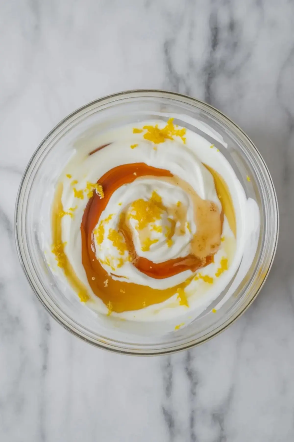 Glass bowl of yogurt topped with lemon curd, honey, and lemon zest for blueberry lemon yogurt bark mixture.