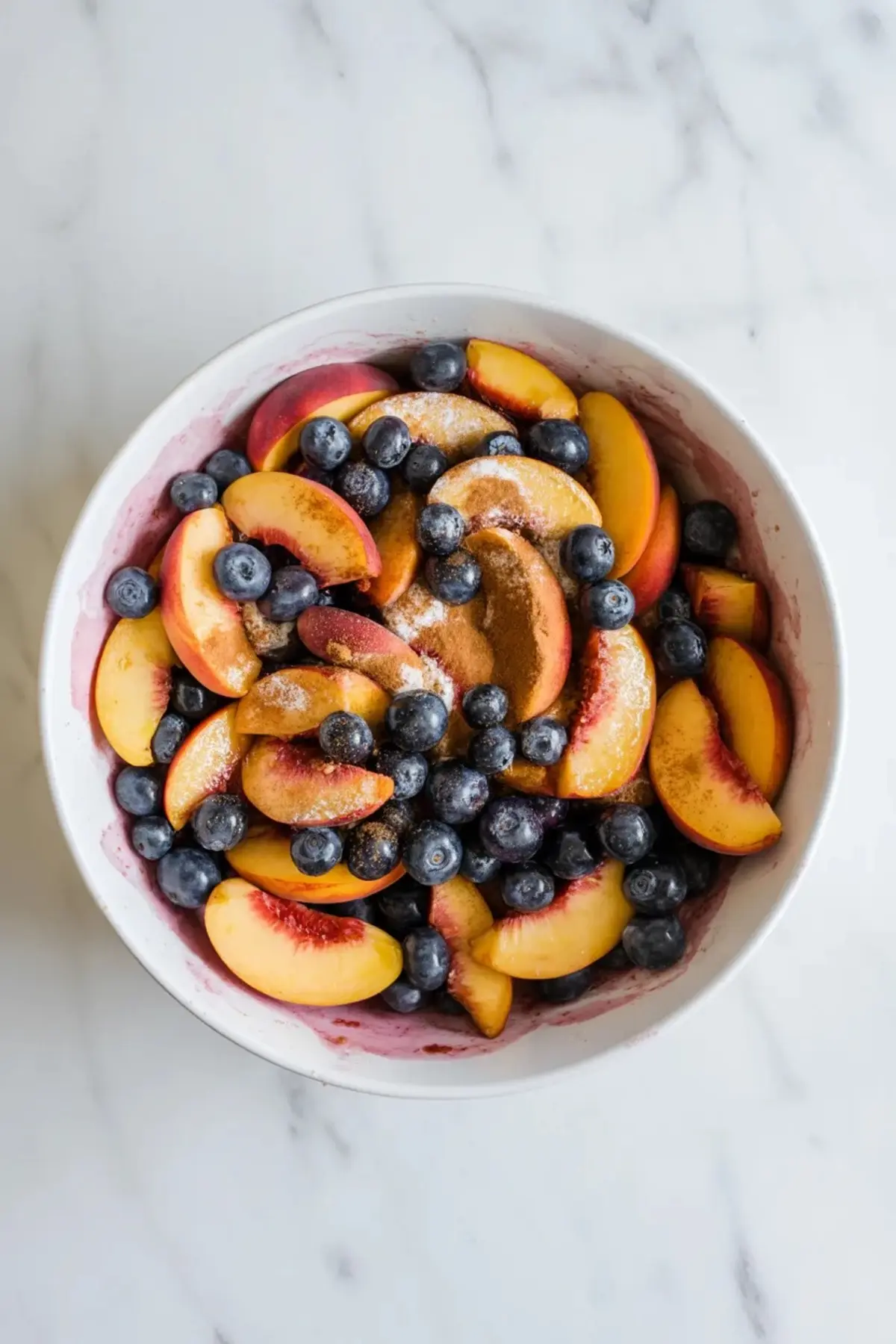 Peaches and blueberries tossed with sugar and cinnamon in a bowl for blueberry peach crisp filling before baking.