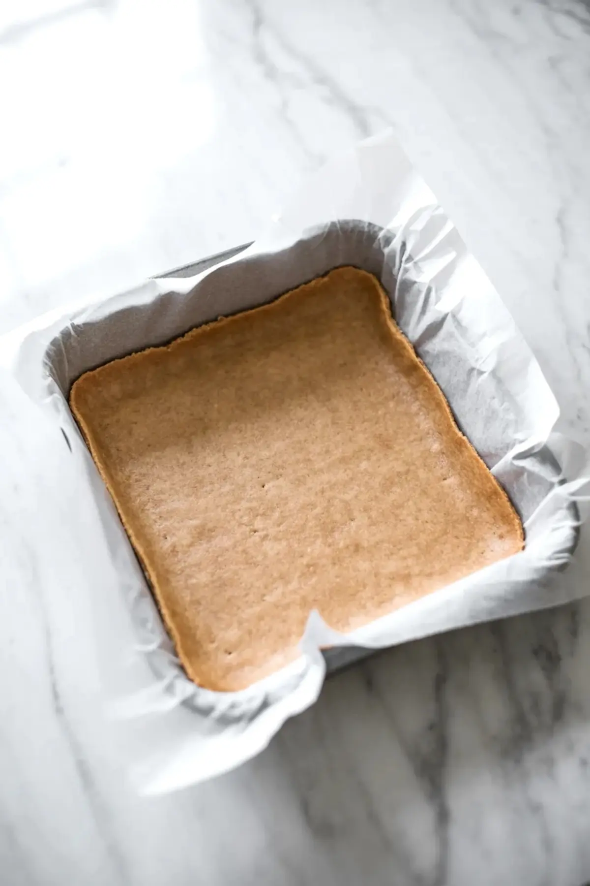 Brown butter lemon bar crust baked in a parchment lined pan before the lemon filling is added.