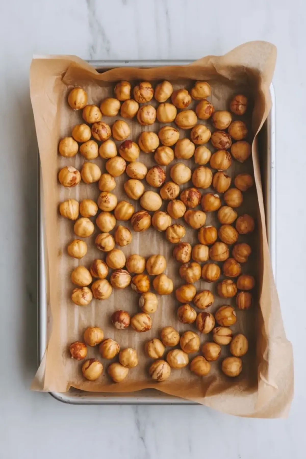 Toasted hazelnuts spread on a parchment lined baking tray for chocolate hazelnut cake filling before they are folded into the chocolate mixture.