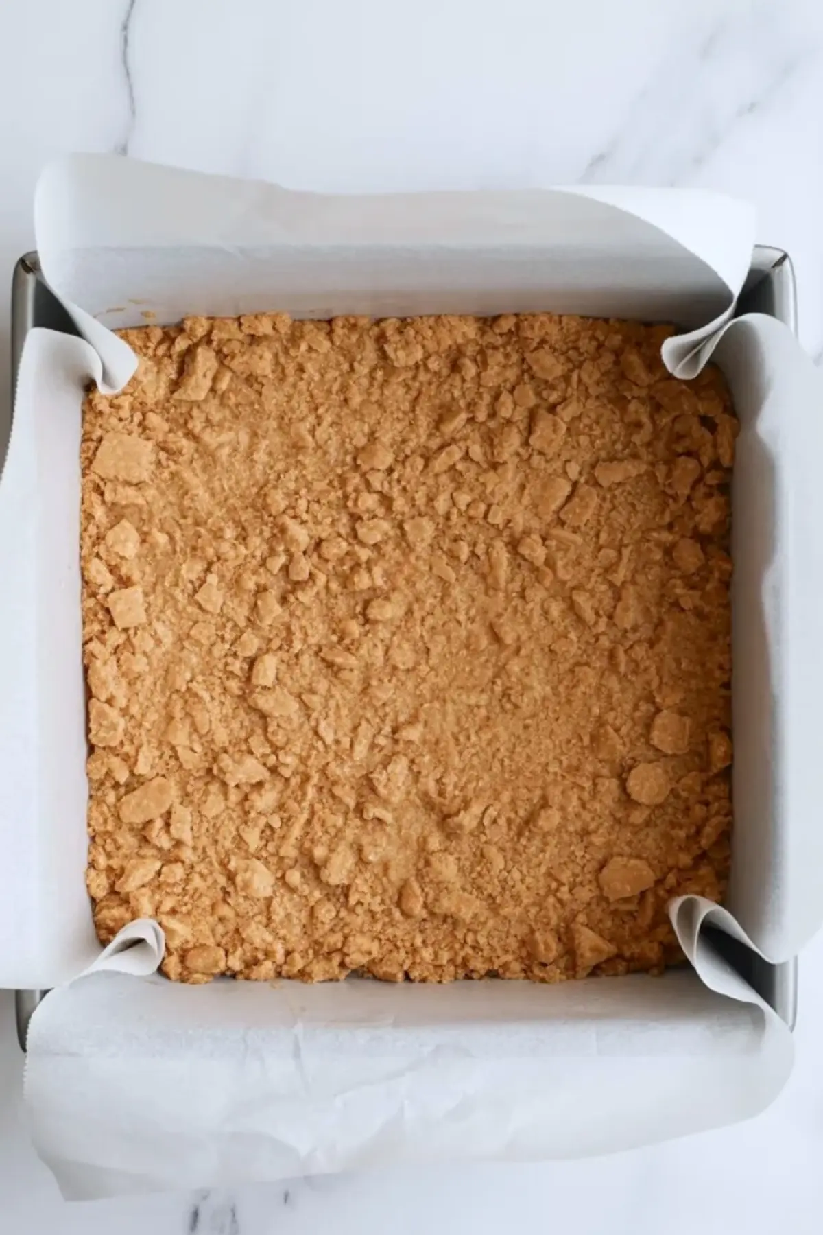 Buttery crust mixture for coconut cream pie bars in a glass bowl on a white marble surface.