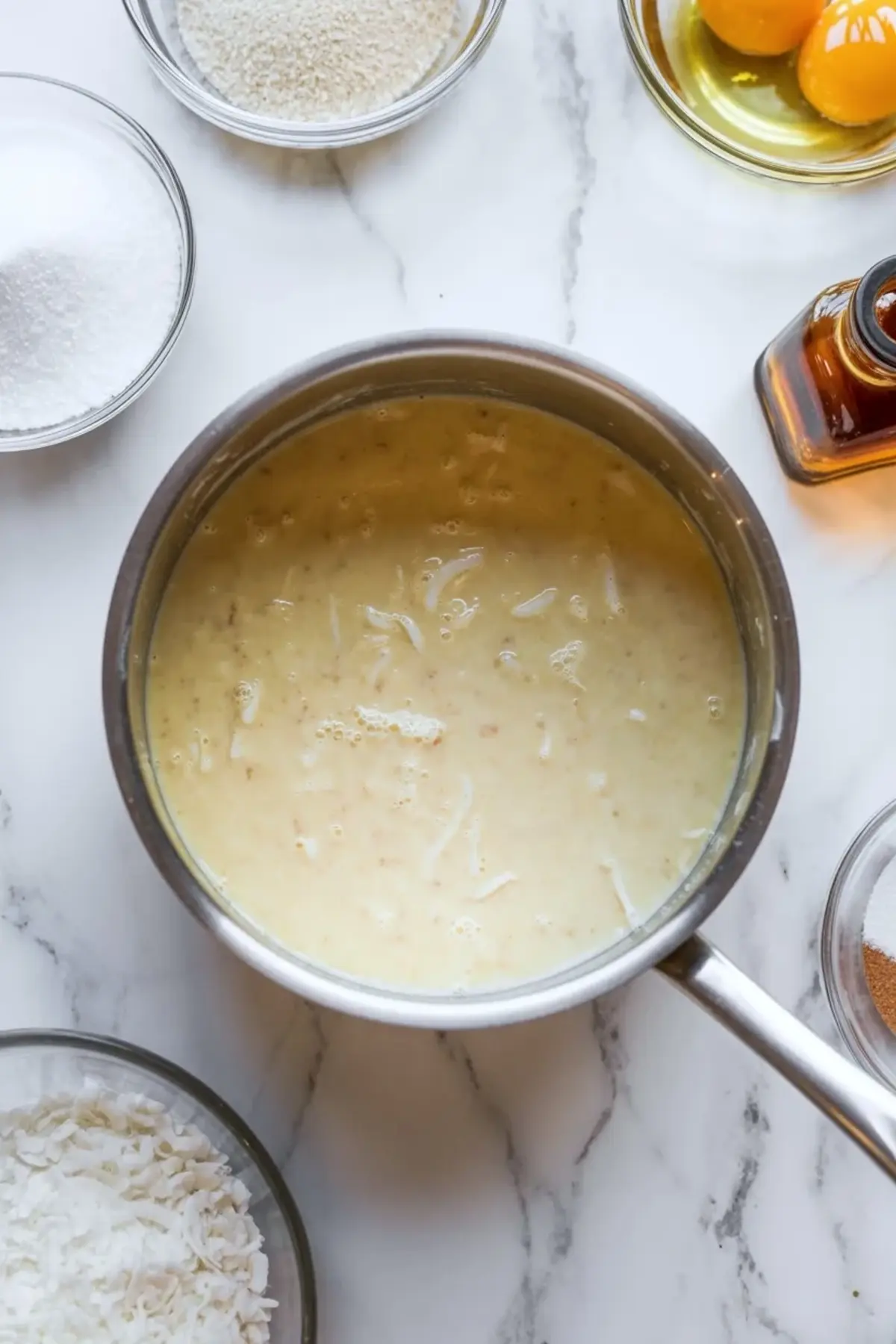 Smooth coconut filling for coconut cream pie bars cooking in a saucepan on a white marble surface.