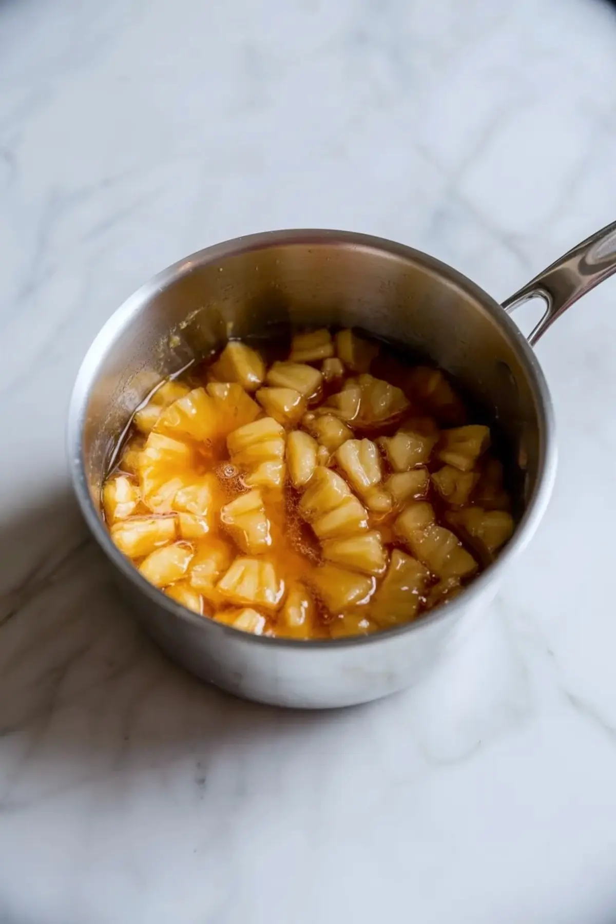 Pineapple topping cooking in a saucepan for coconut pineapple cream pie bars with glossy fruit pieces and syrup.