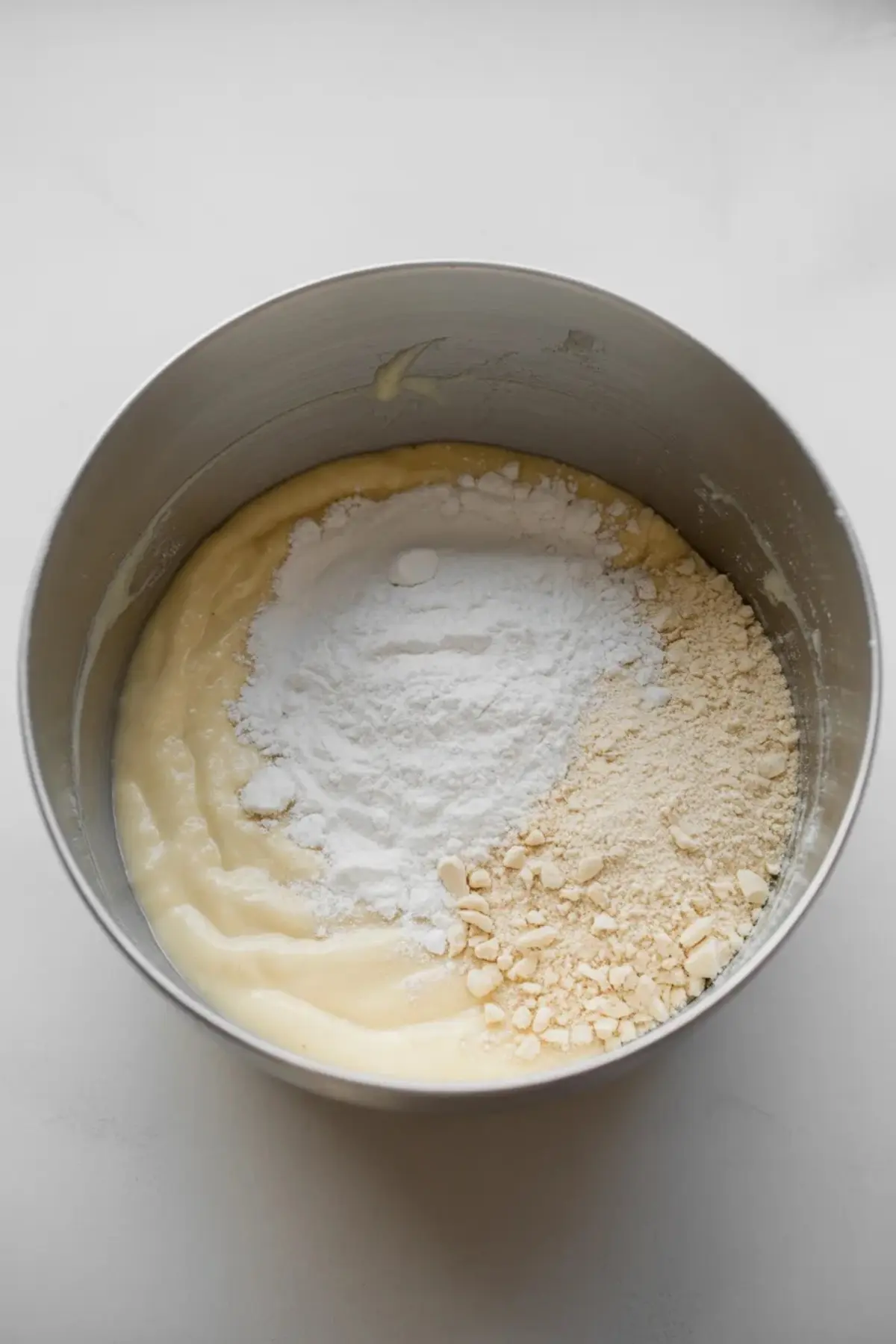 Bowl with frangipane cream filling base topped with almond flour and flour before mixing, showing the stage just before the almond filling is fully combined.