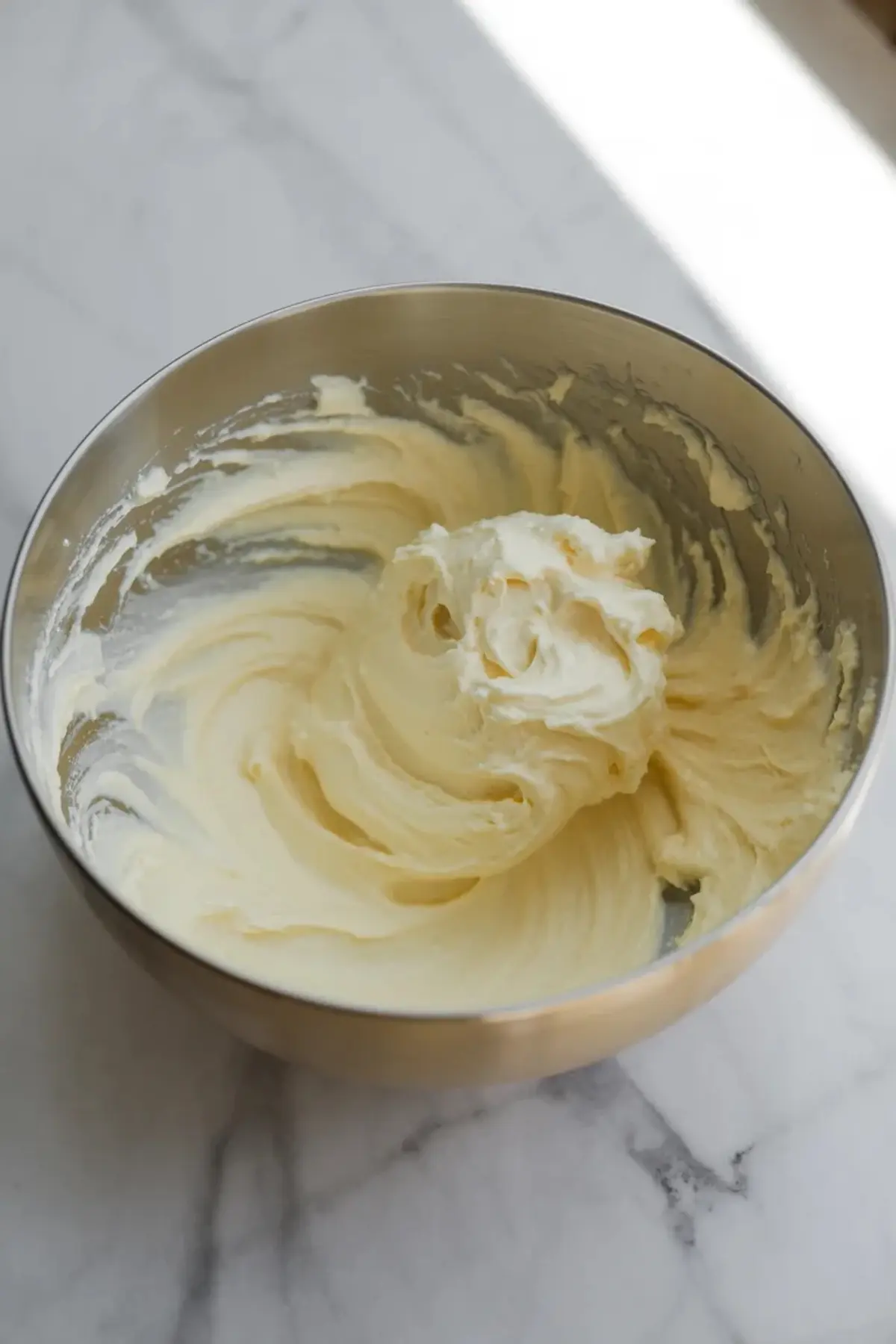 Creamed butter and sugar for frangipane cream filling whipped in a metal bowl until pale and fluffy, showing the smooth base that gives the almond filling its texture.