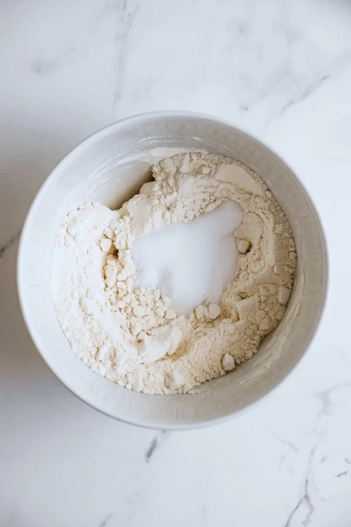 Flour and sugar mixture for the crust and crumb topping of lemon blueberry crumb bars in a white bowl on white marble.