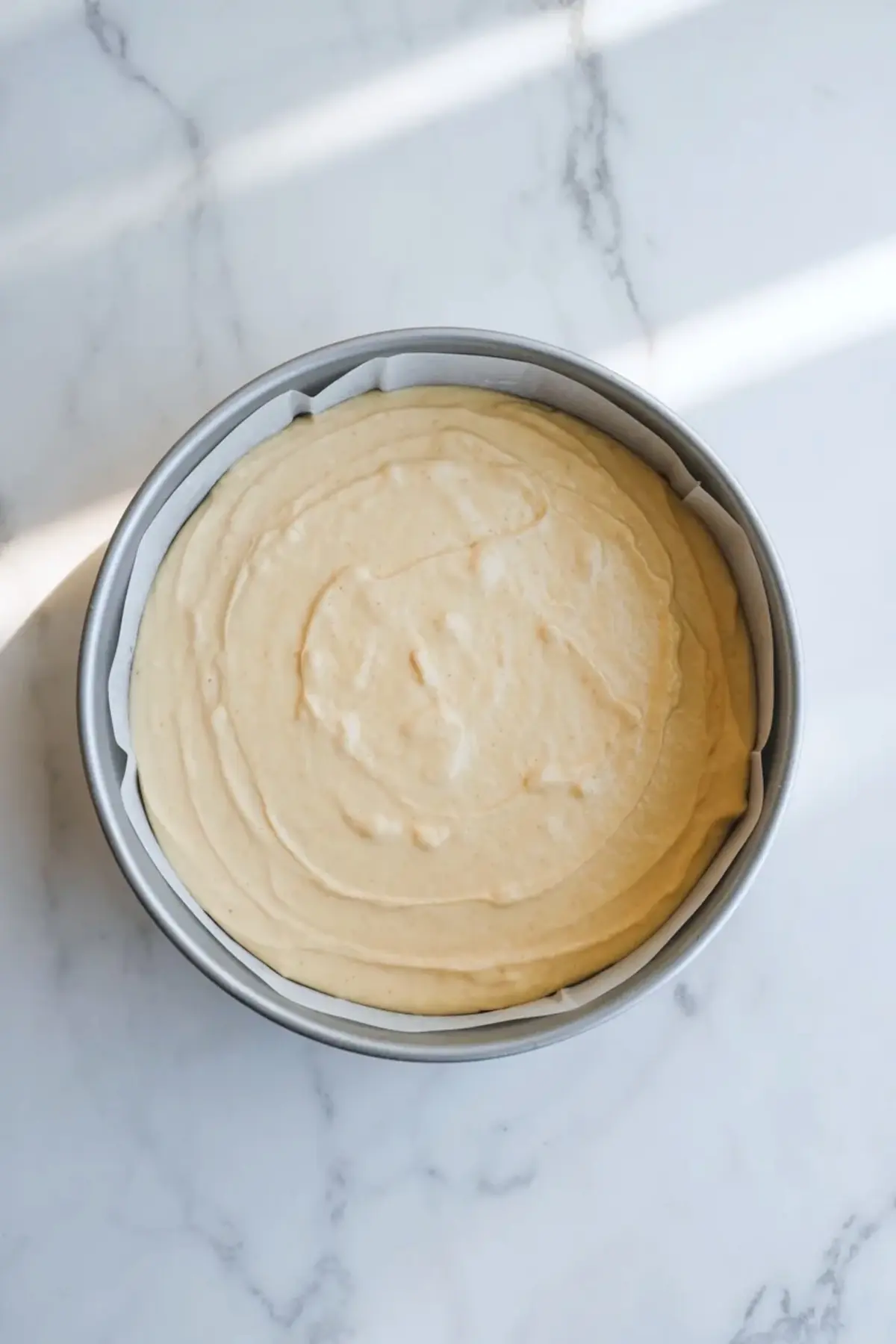 Lemon olive oil cake batter smoothed in a round cake pan lined with parchment before baking.