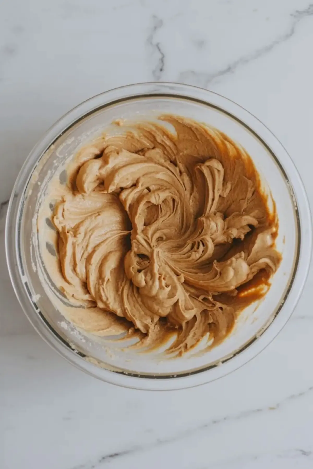 Maple frosting whipped in a glass bowl for maple bacon cupcakes.