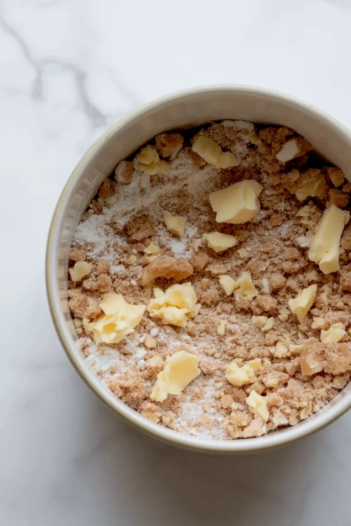 Crumble topping mixture with butter pieces in a bowl for mini peach cobbler cheesecakes before baking.