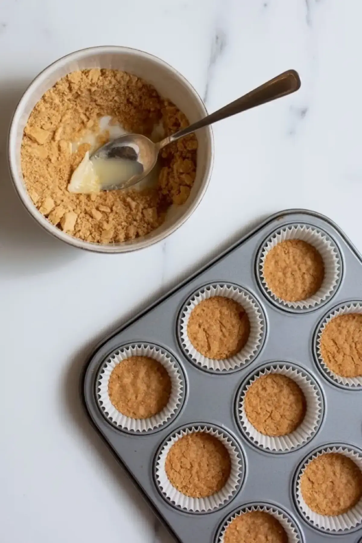 Graham cracker crust being pressed into cupcake liners in a muffin tin for mini peach cobbler cheesecakes.